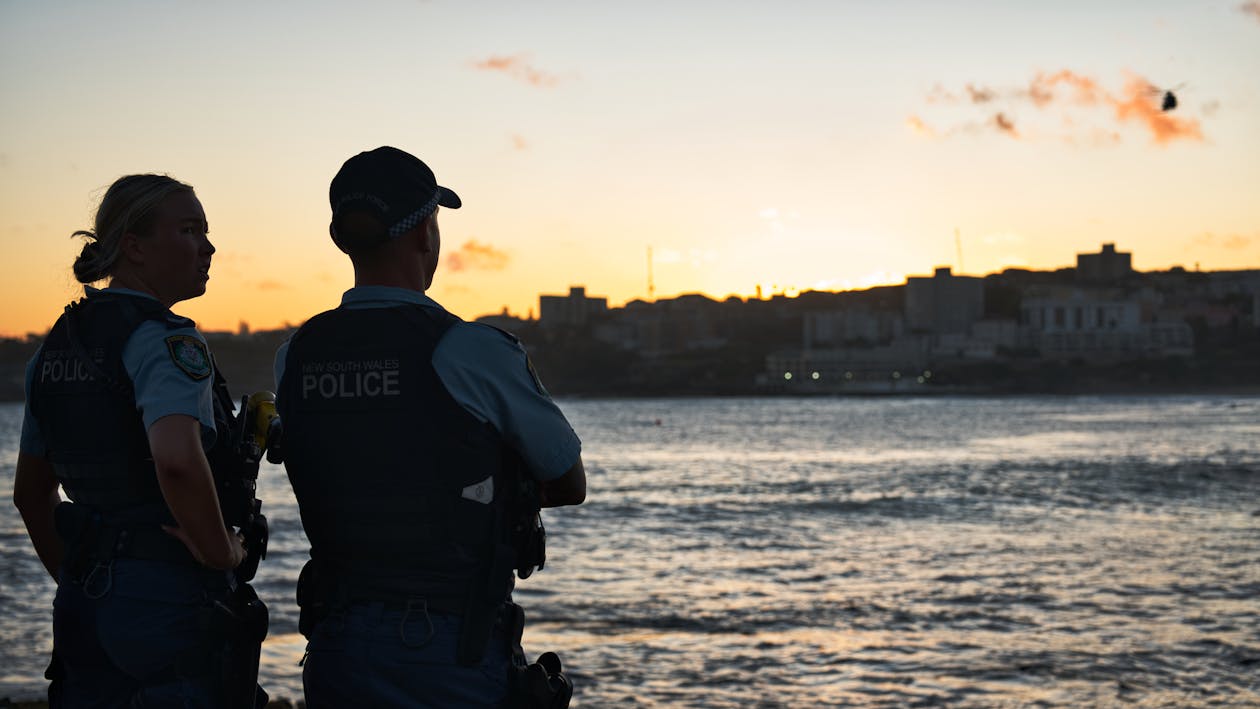 Two Australian police officers in uniform standing at Bondi Beach at sunset overlooking the city
