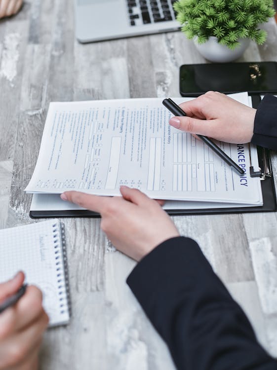 Close-up of hands reviewing an insurance policy document on a clipboard, with a pen and notepad beside a laptop