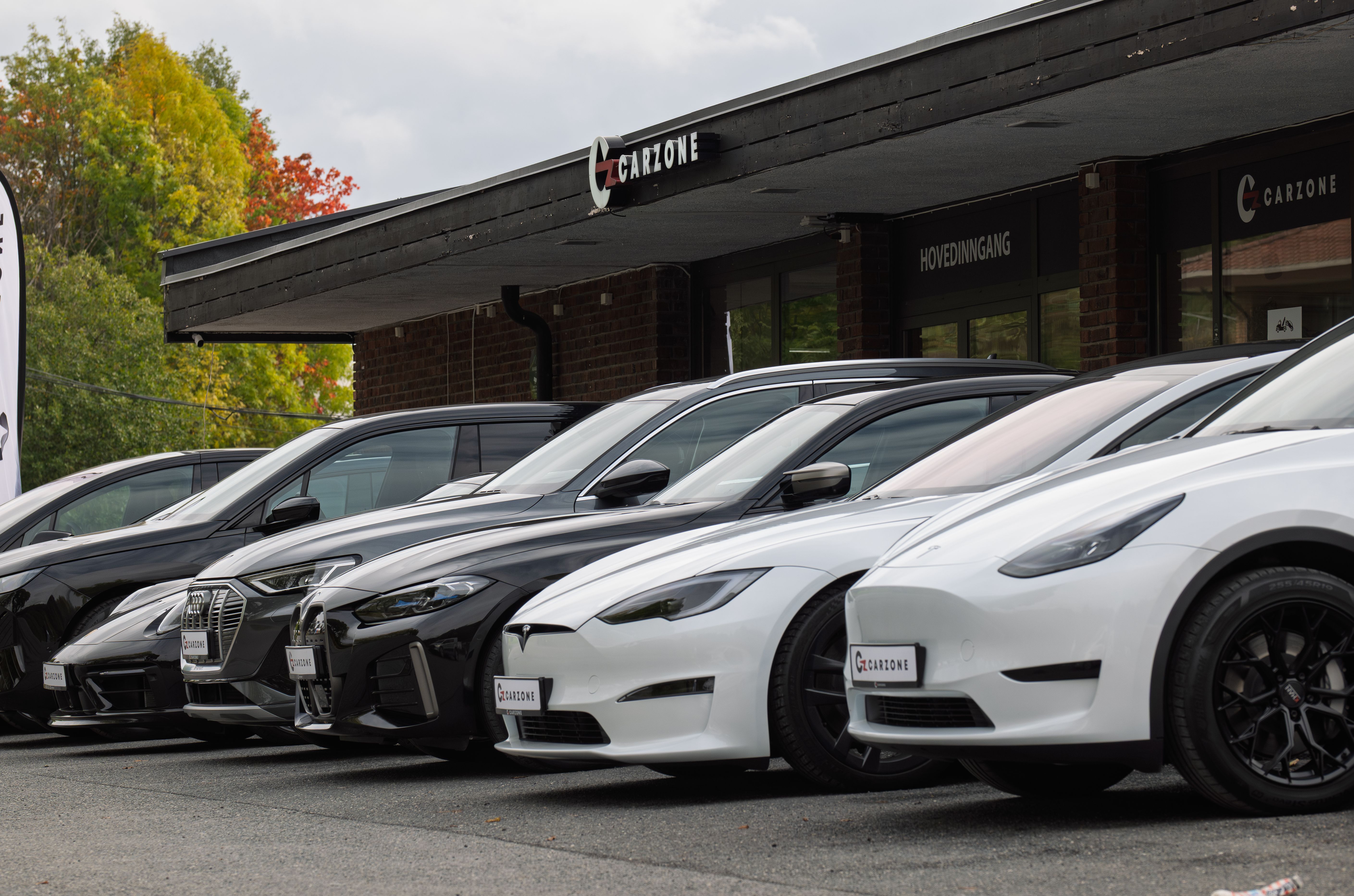 Bruktbiler hos Carzone på Høvik – Tesla Model Y, BMW i4, ix, Audi e-tron og tesla model s foran Carzone-bygget en høstdag 2025.