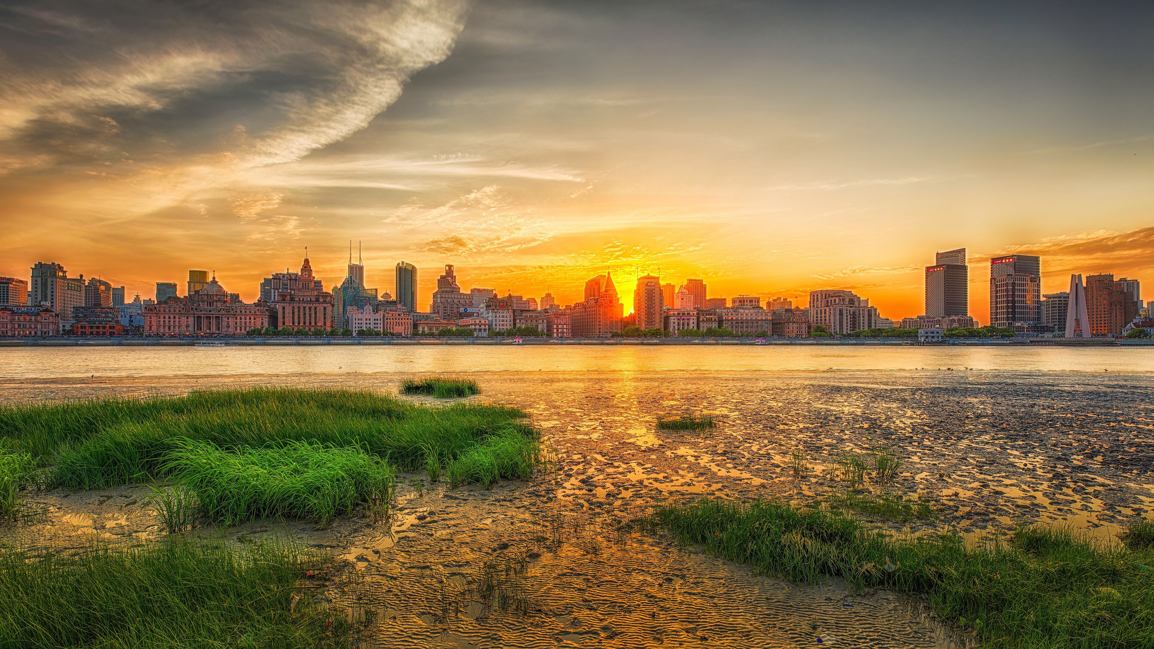 The colonial-era buildings of the Bund lined up along the Huangpu River at sunset, seen from the Pudong bank