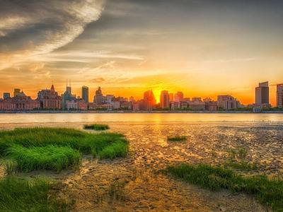 The colonial-era buildings of the Bund lined up along the Huangpu River at sunset, seen from the Pudong bank