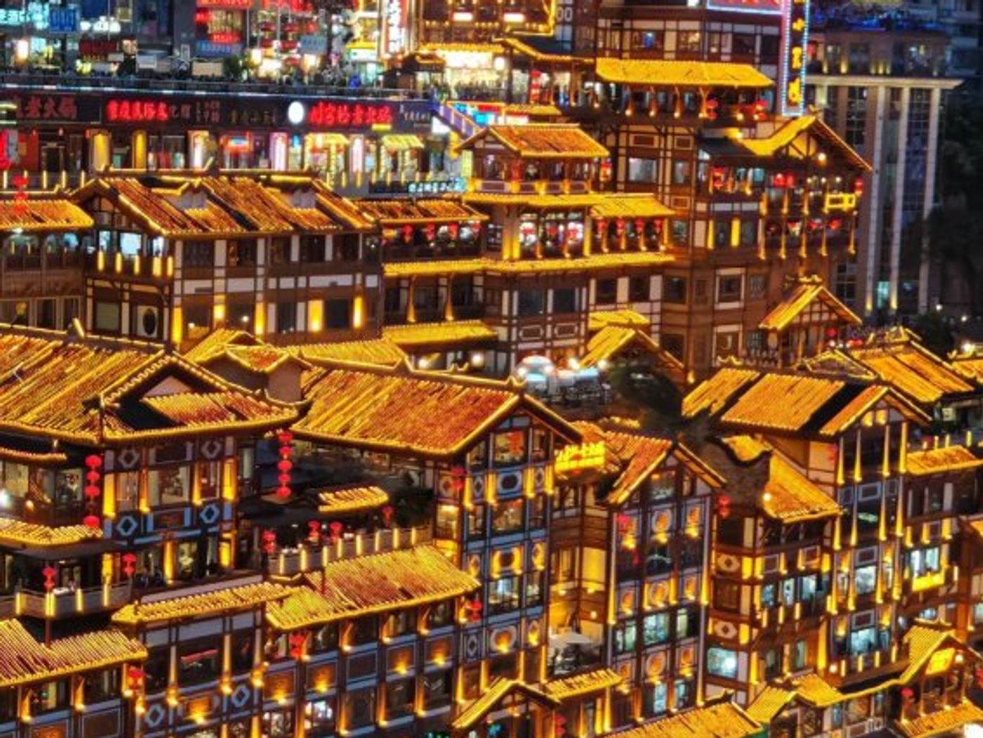 Tiers of golden-lit wooden stilt houses at Hongyadong stacked up the hillside at night, with the red 洪崖洞 sign and crowds below