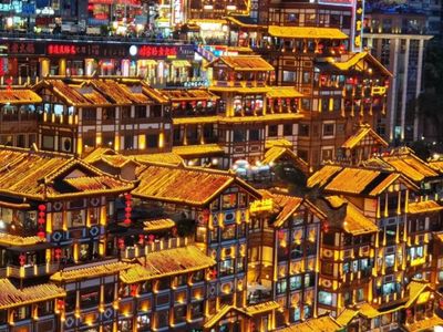 Tiers of golden-lit wooden stilt houses at Hongyadong stacked up the hillside at night, with the red 洪崖洞 sign and crowds below