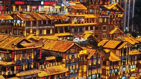 Tiers of golden-lit wooden stilt houses at Hongyadong stacked up the hillside at night, with the red 洪崖洞 sign and crowds below