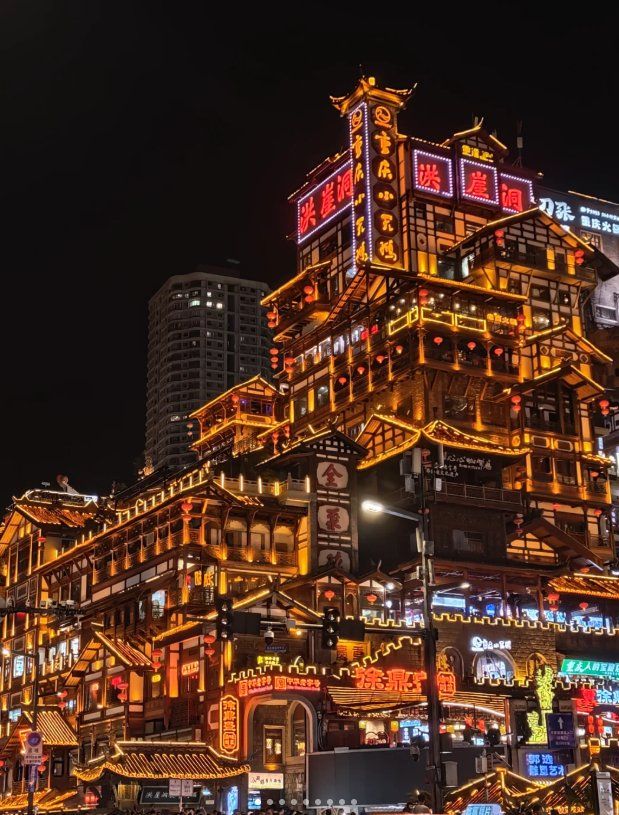Hongyadong's stacked stilt buildings glowing gold at night, with neon 洪崖洞 signs on the top tower and a modern high-rise behind
