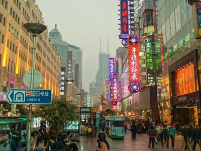 Neon signs lighting up East Nanjing Road pedestrian street at dusk, with shoppers and the sightseeing tram