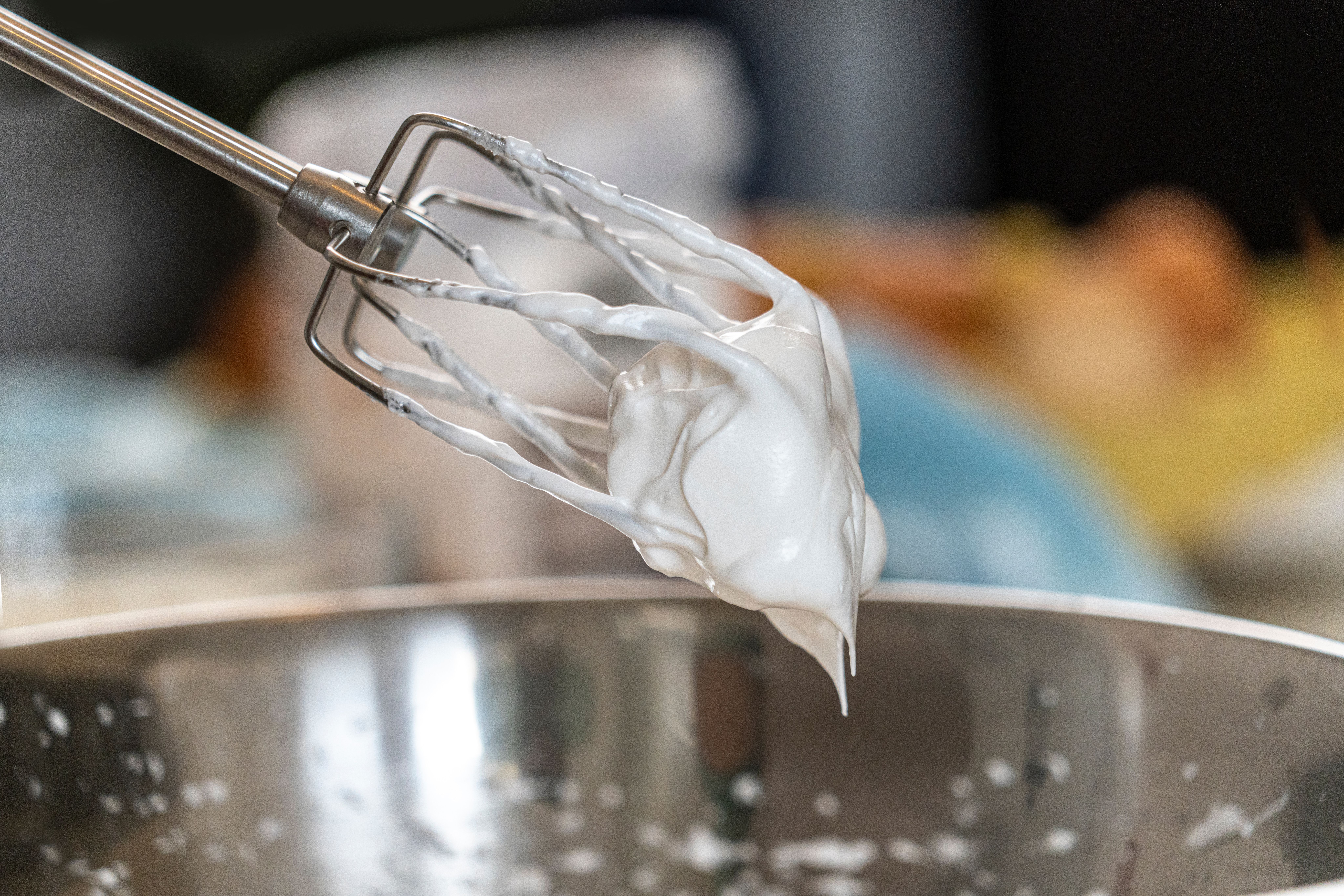 The whisks of a mixer with some cream dripping from it