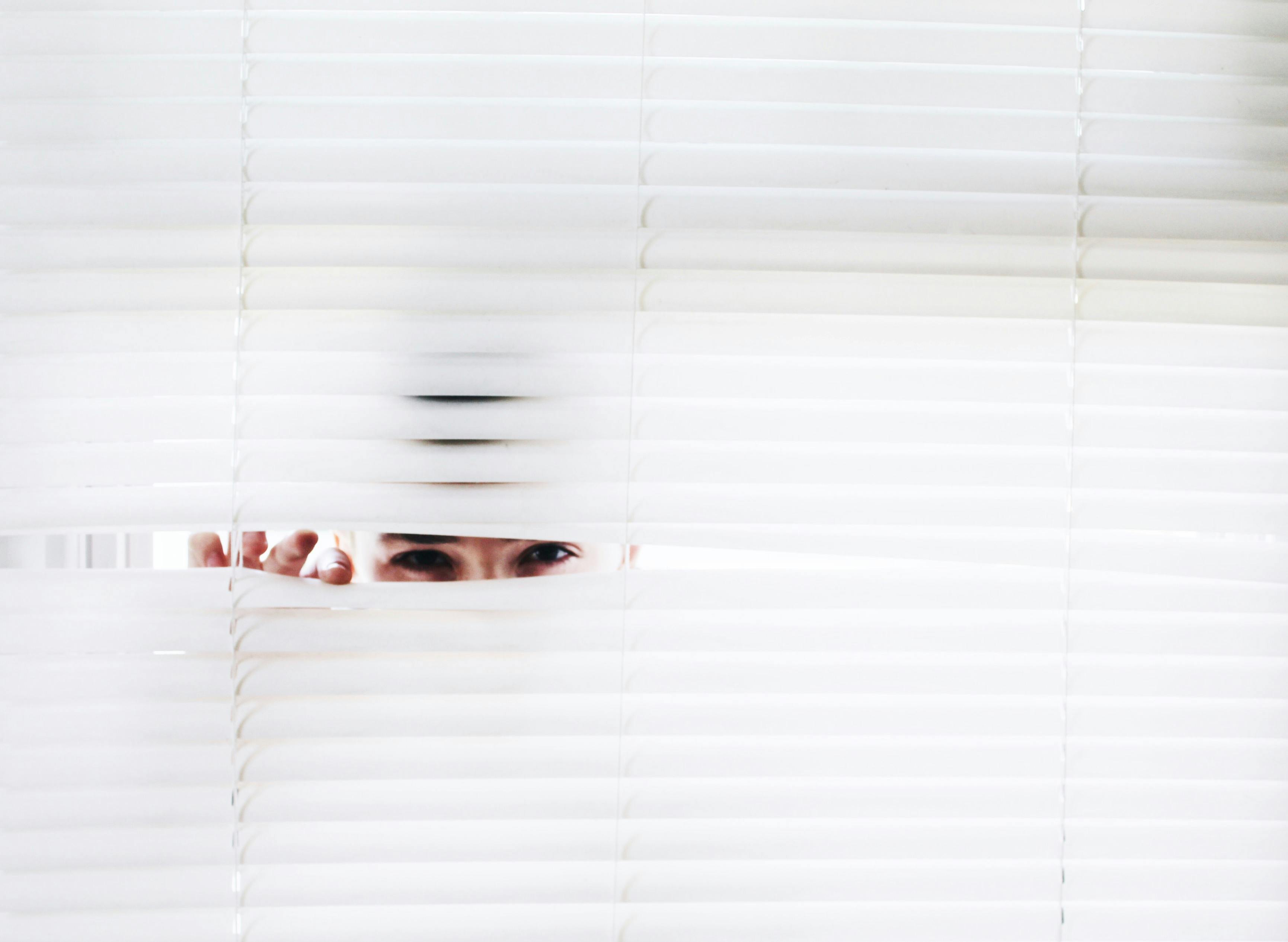 A person peaking through window blinds.