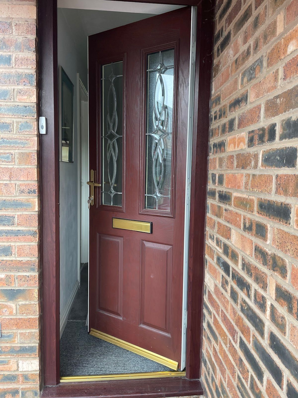 Burgundy composite front door with decorative glass panel on a UK brick house, ready for a spring security check