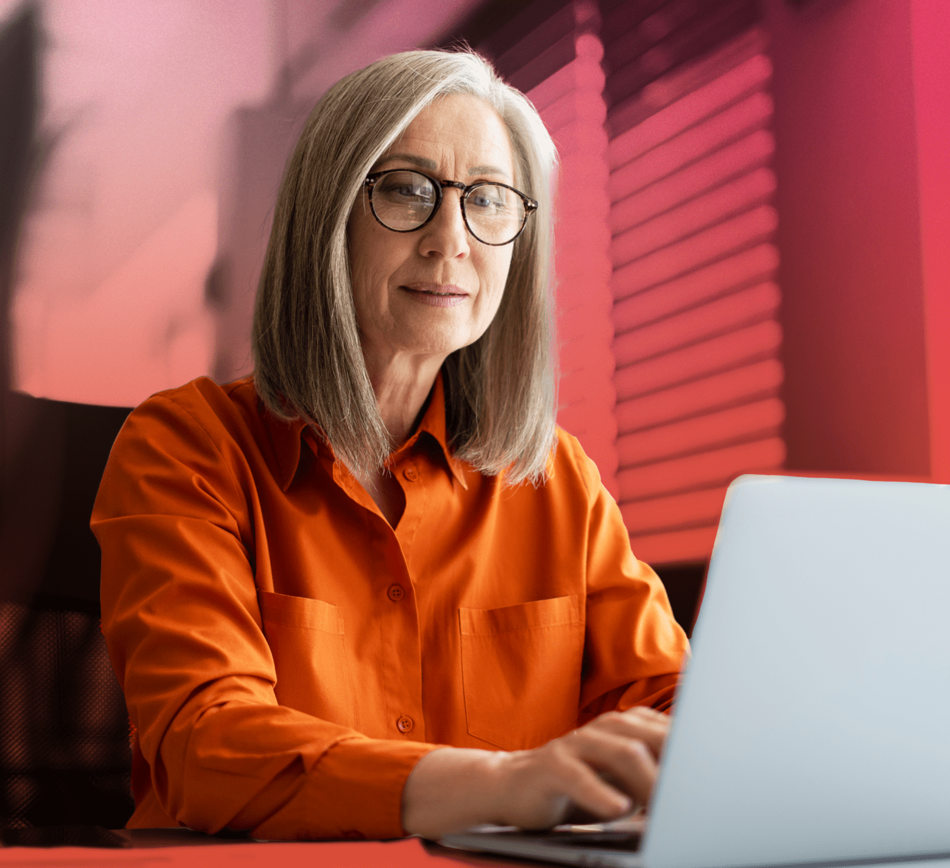 woman in an orange shirt working on laptop to learn what digital assets are, on a pink background.
