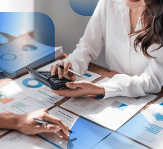 Digital asset management (DAM) trends reports laid out on a desk with women's hand holding a pen pointing at paper, second women holding a calculator looking at a document with blue overlay