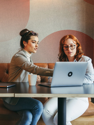 Two women working on a laptop in a cafe space with a cup of coffee on the table