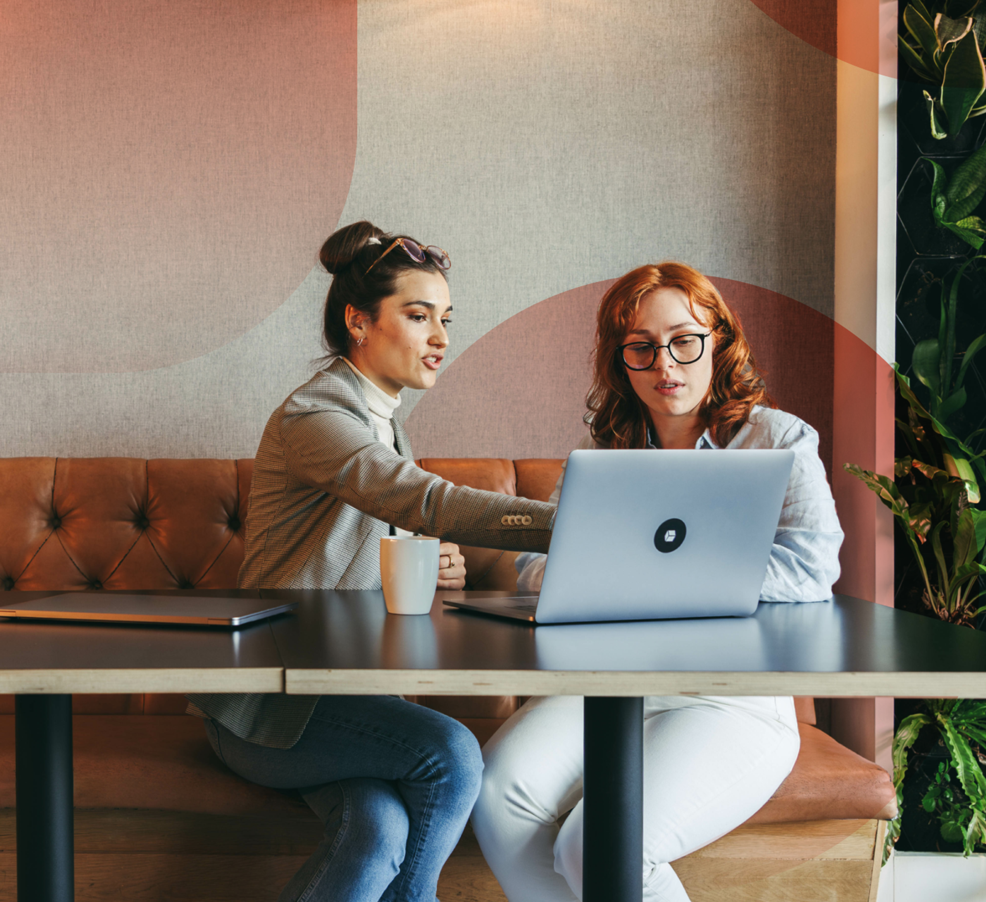 Two women working on a laptop in a cafe space with a cup of coffee on the table