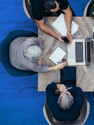 group of people working together with a laptop, tablet and notebooks on a wooden table over a blue background