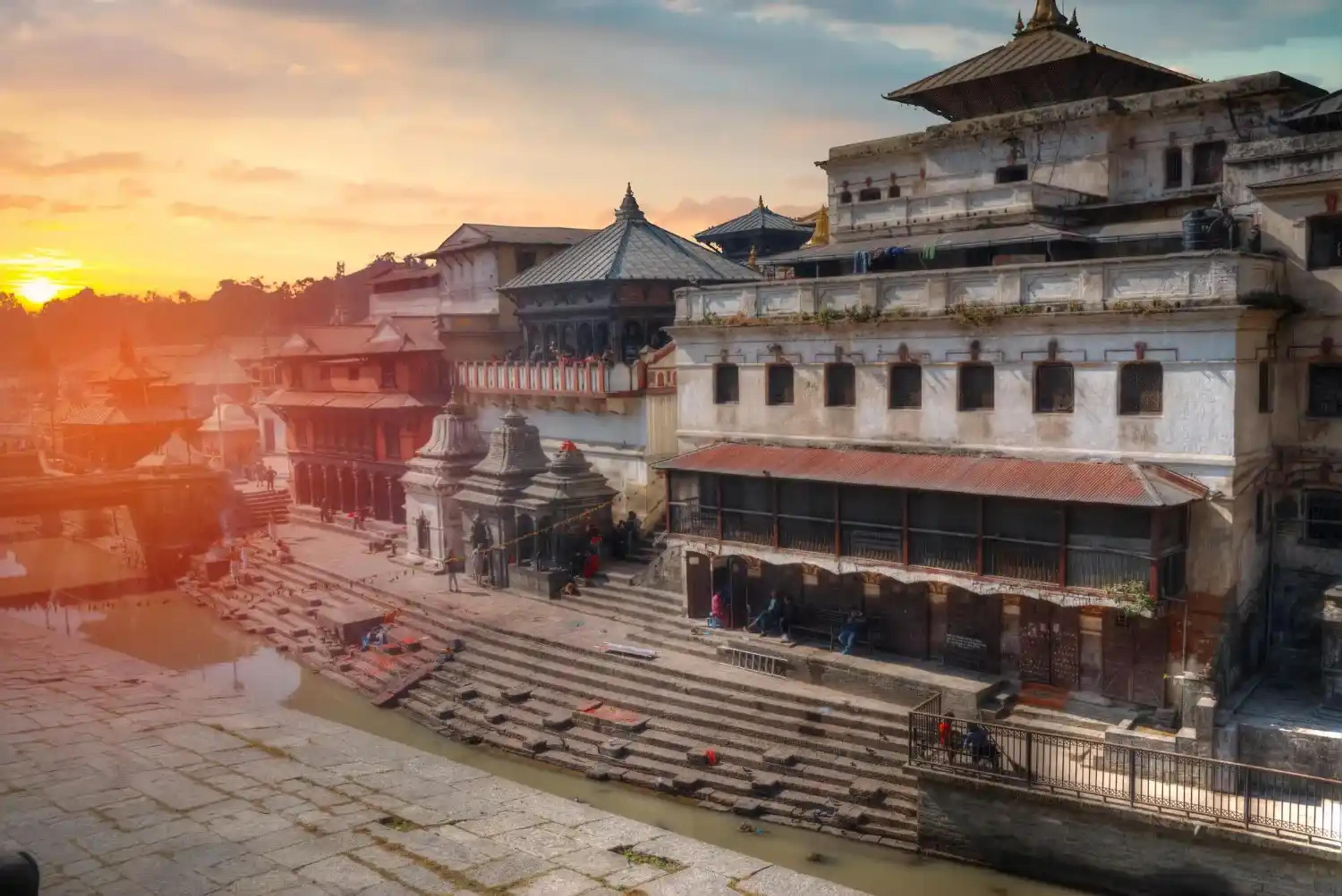 The ancient stone ghats of the Pashupatinath Temple complex along the Bagmati River in Kathmandu, beautifully illuminated by the warm, golden glow of the setting sun.