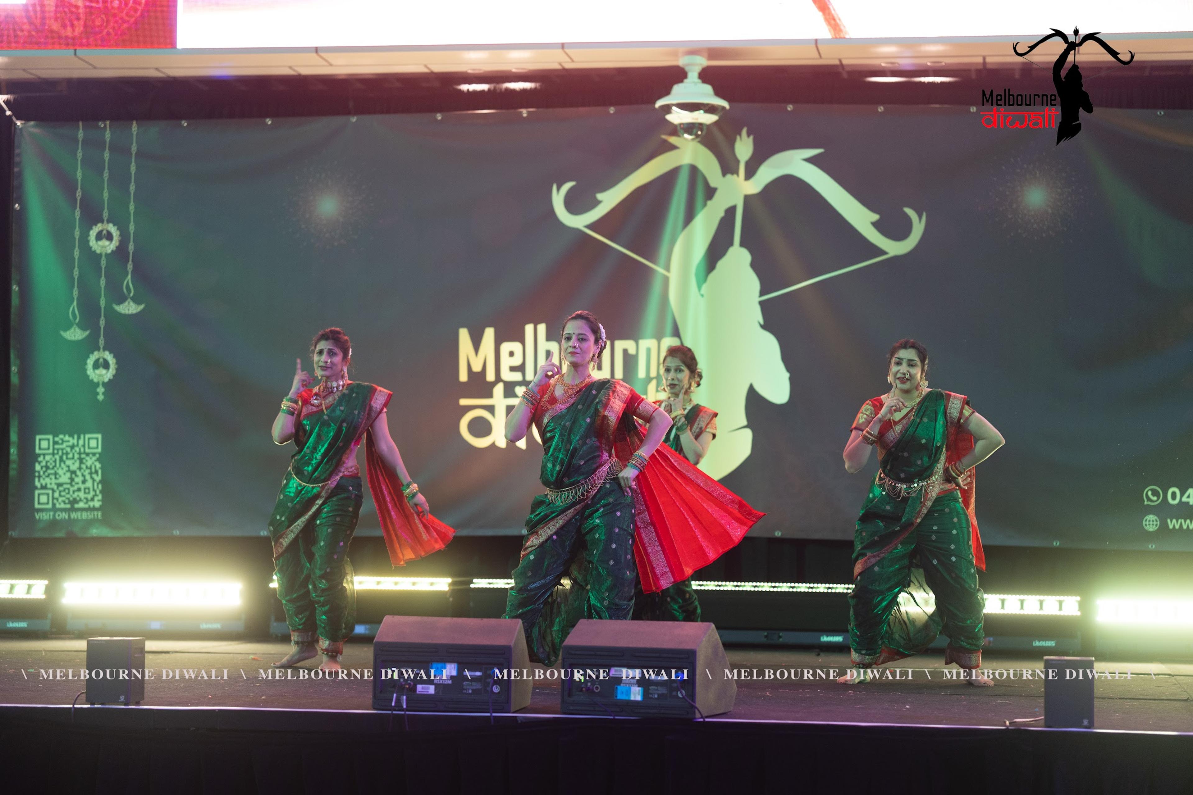 A folk dance troupe in green and red saris performing on the main stage at Melbourne Diwali 2025
