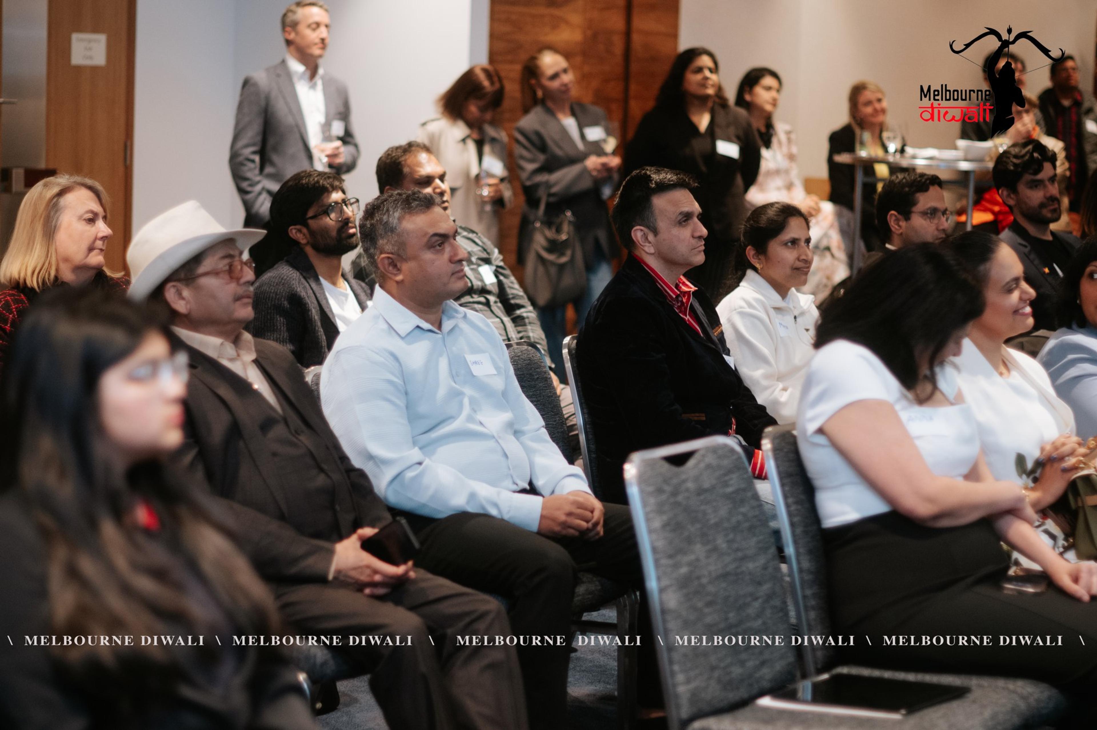 Guests in the audience, one in a white hat, listen to a speaker