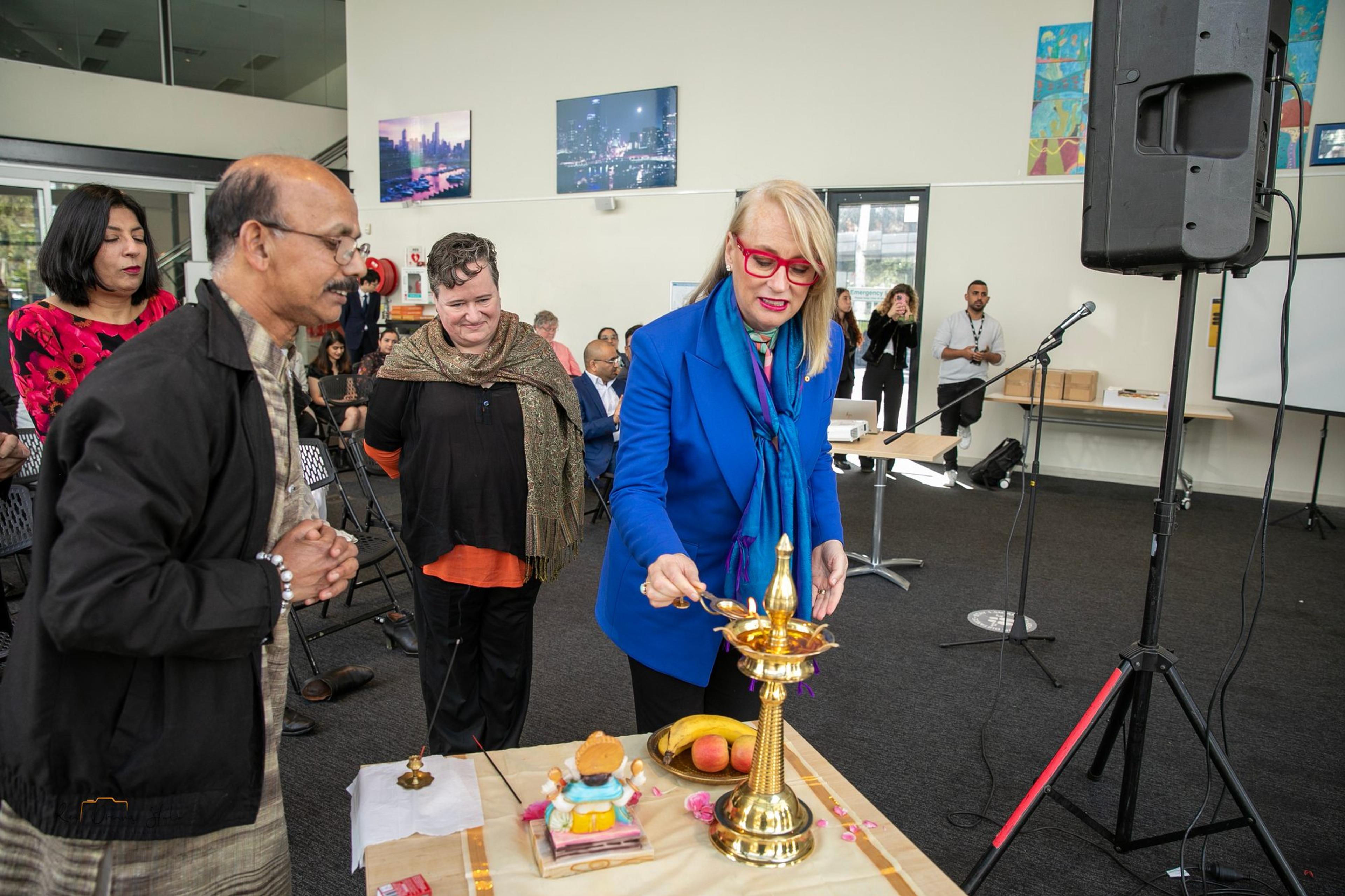 A guest in a blue jacket lights the brass lamp as others watch