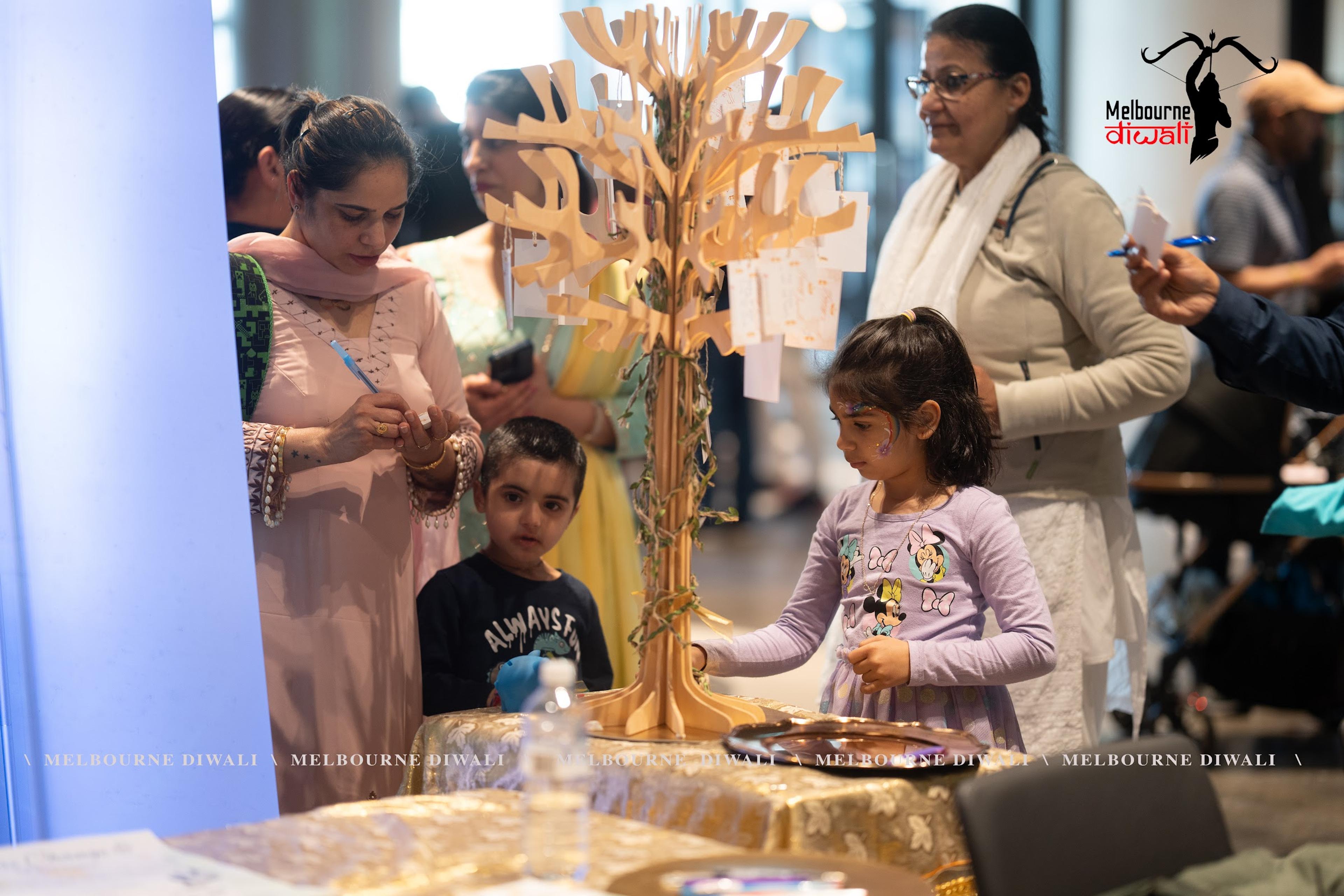 Families gathered around the golden blessing tree at Melbourne Diwali 2025, children tying wishes to its branches