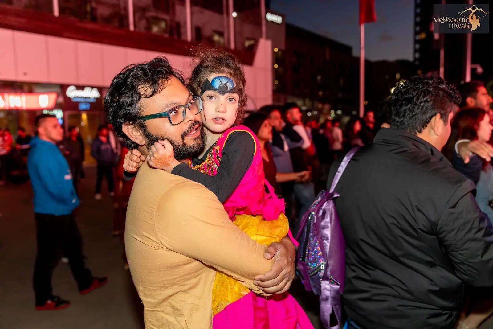 An adult holding a child among evening festival visitors at Melbourne Diwali 2023