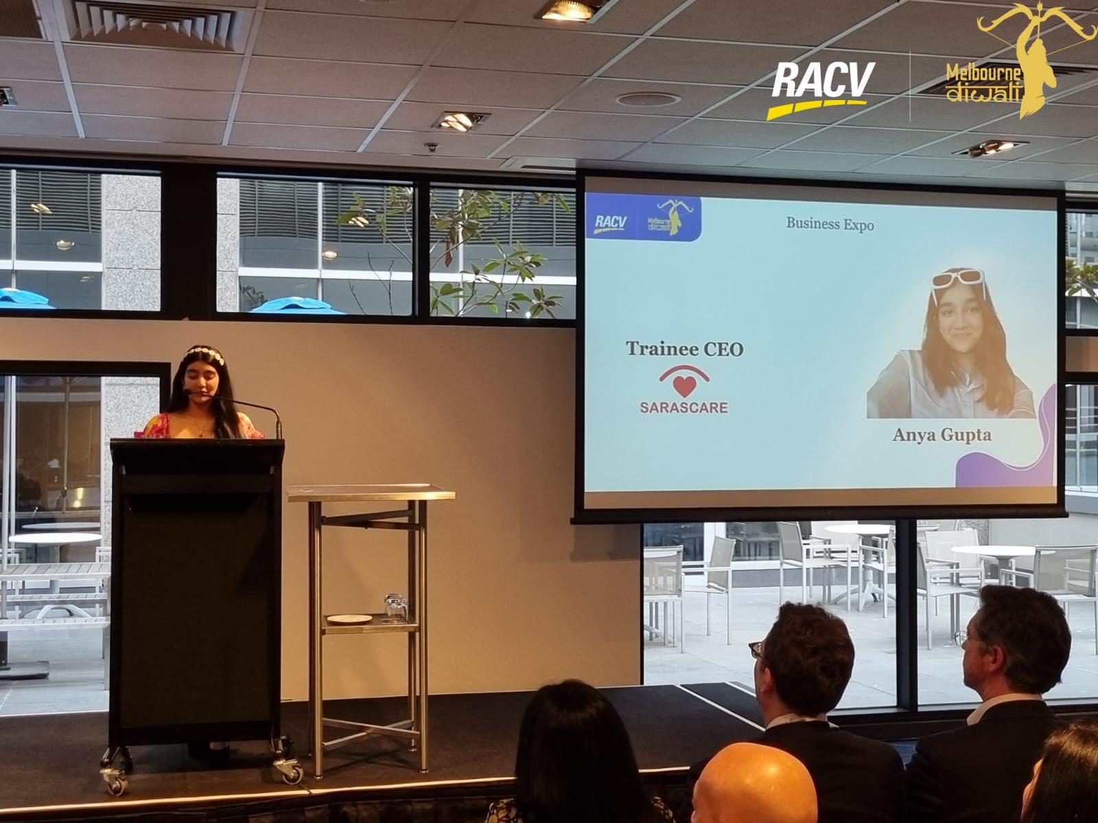 Anya Gupta presents the Business Expo at the lectern beside her name slide