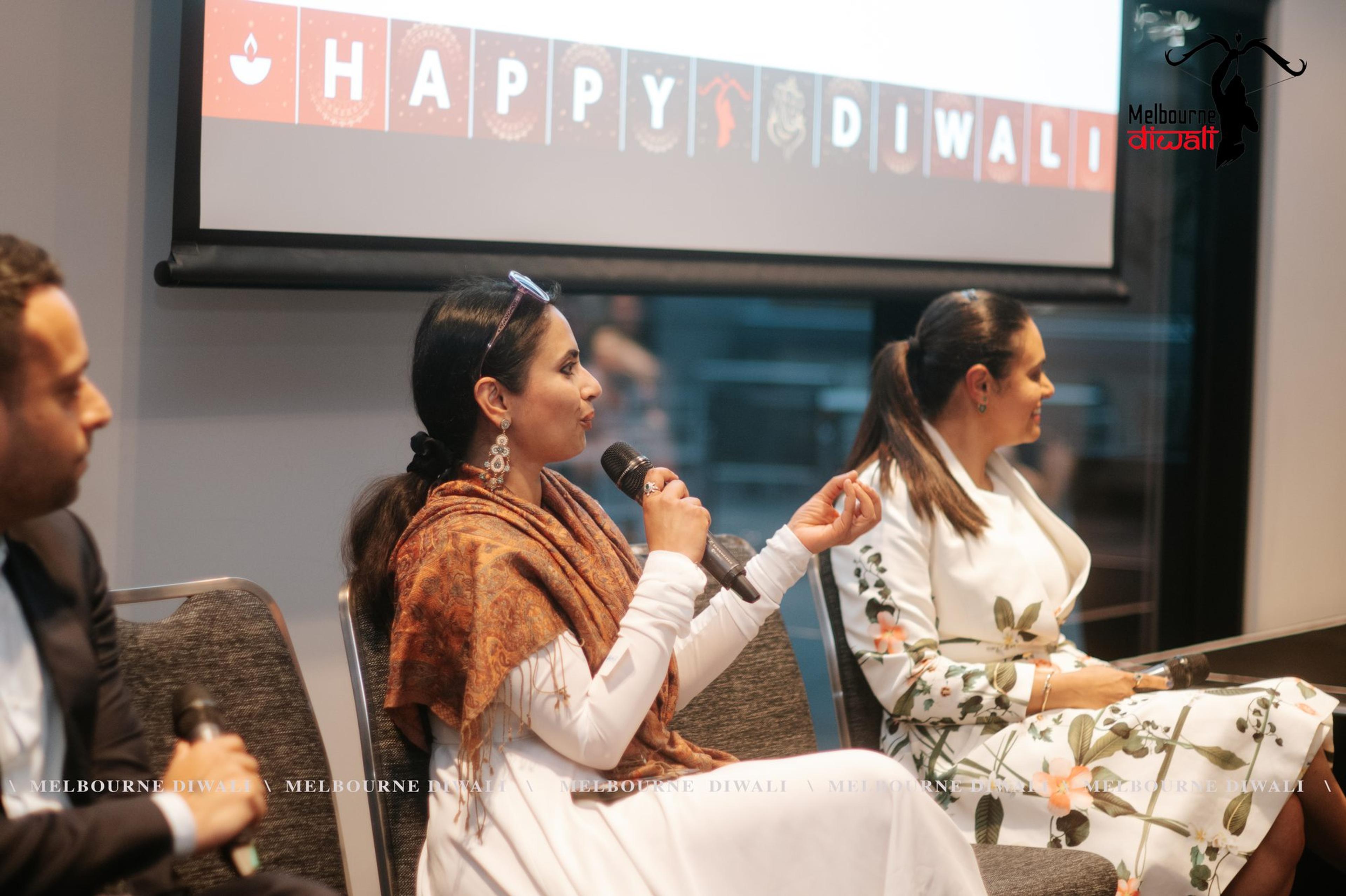 Speakers seated for the Q&A answer questions with handheld microphones under the Happy Diwali screen