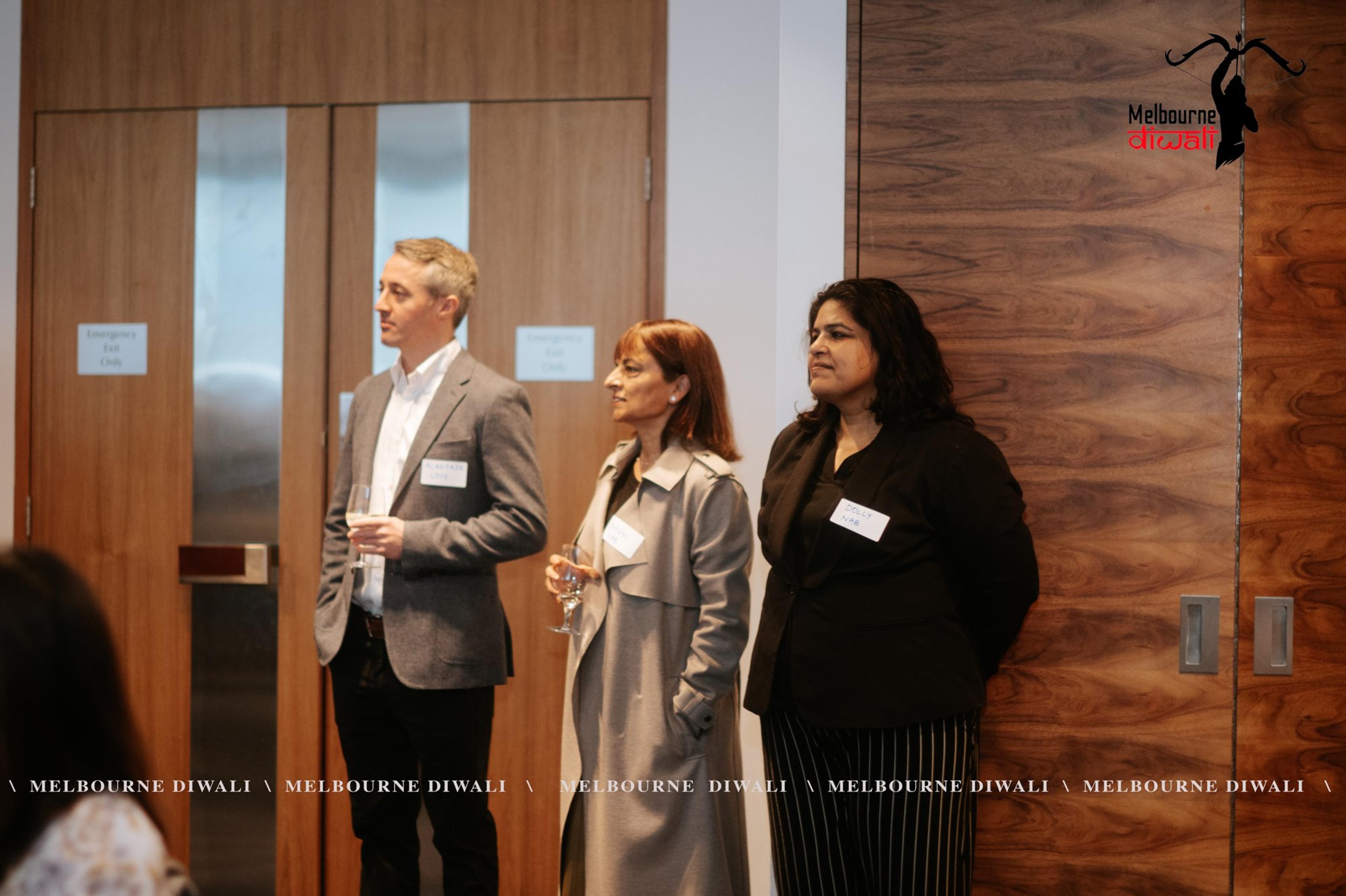 Three guests with name badges stand by the doors at the back of the room