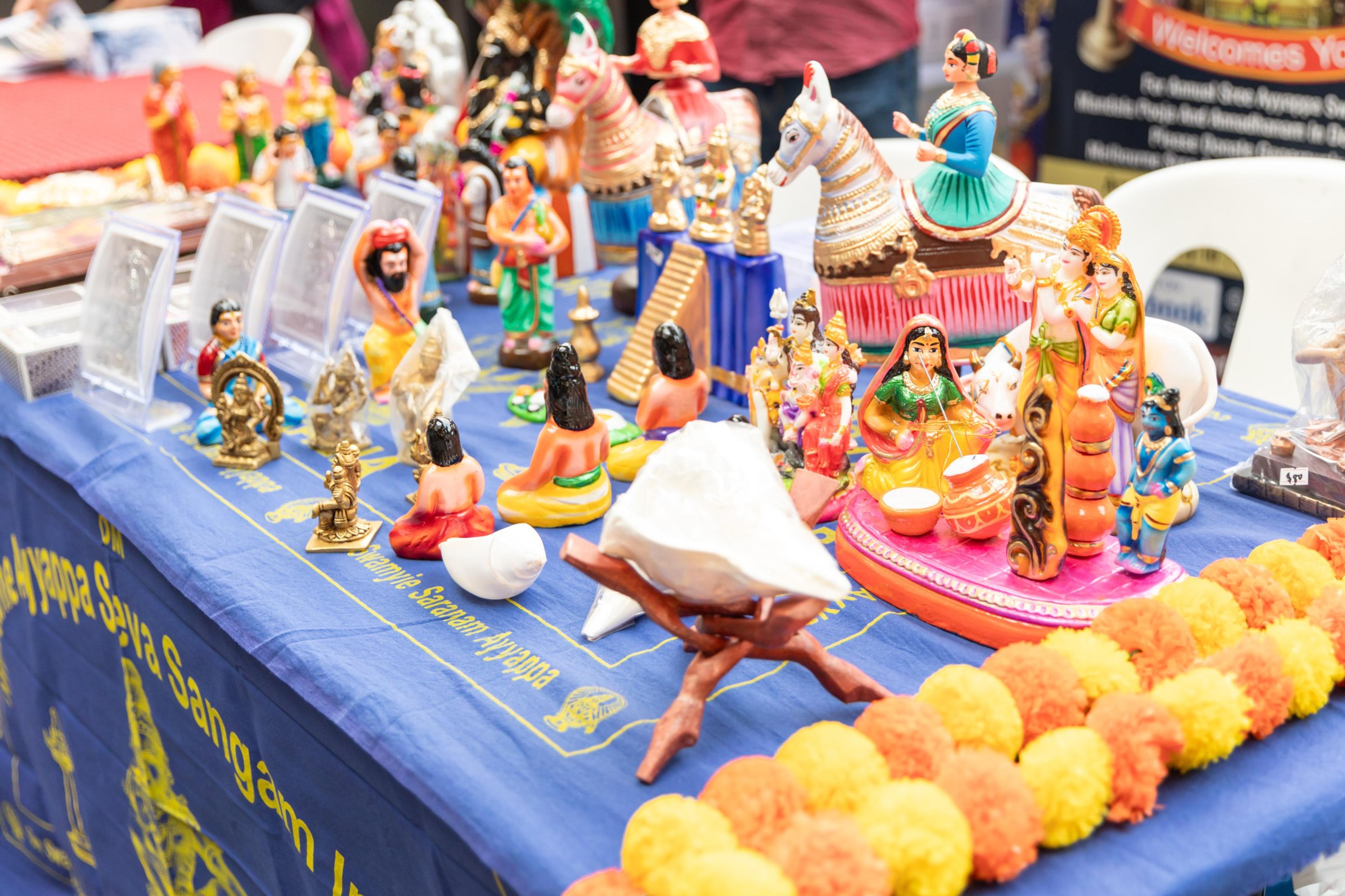 A festive kolu display of painted clay dolls, a conch shell and orange and yellow marigold garlands on a table at Melbourne Diwali