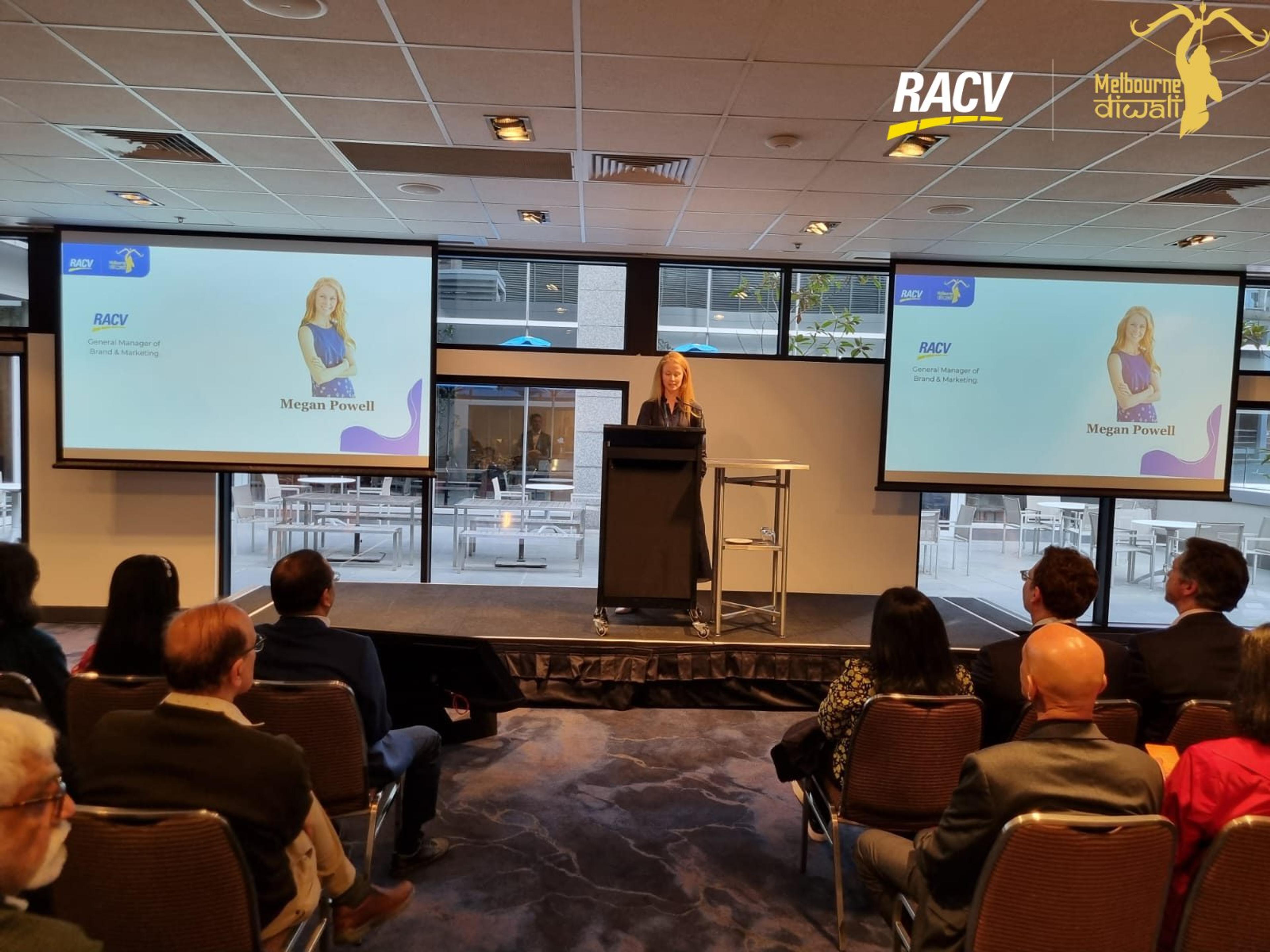 Megan Powell of RACV at the lectern, with her name slide on the twin screens