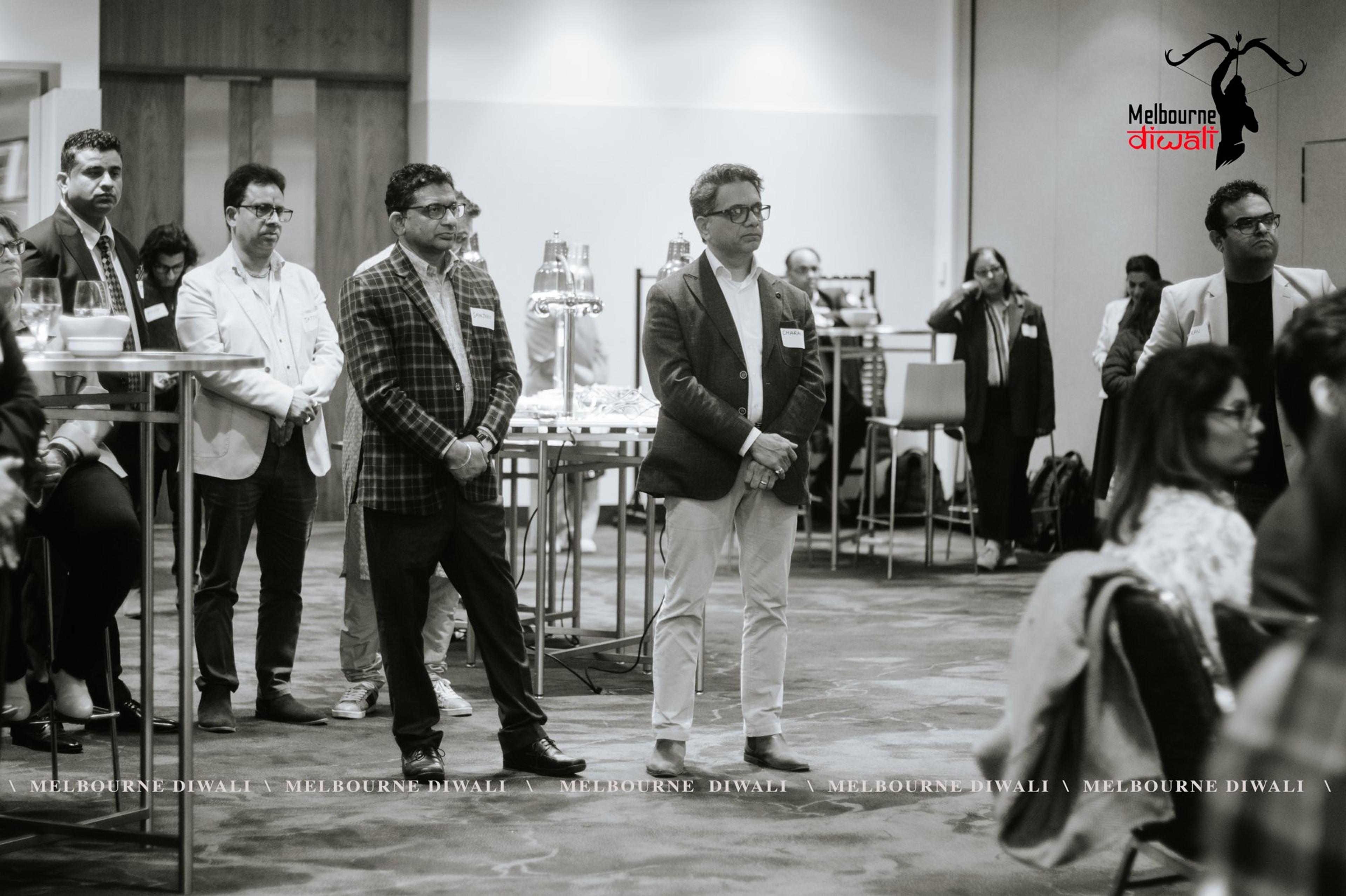 Guests stand at the back of the room during the programme, in black and white