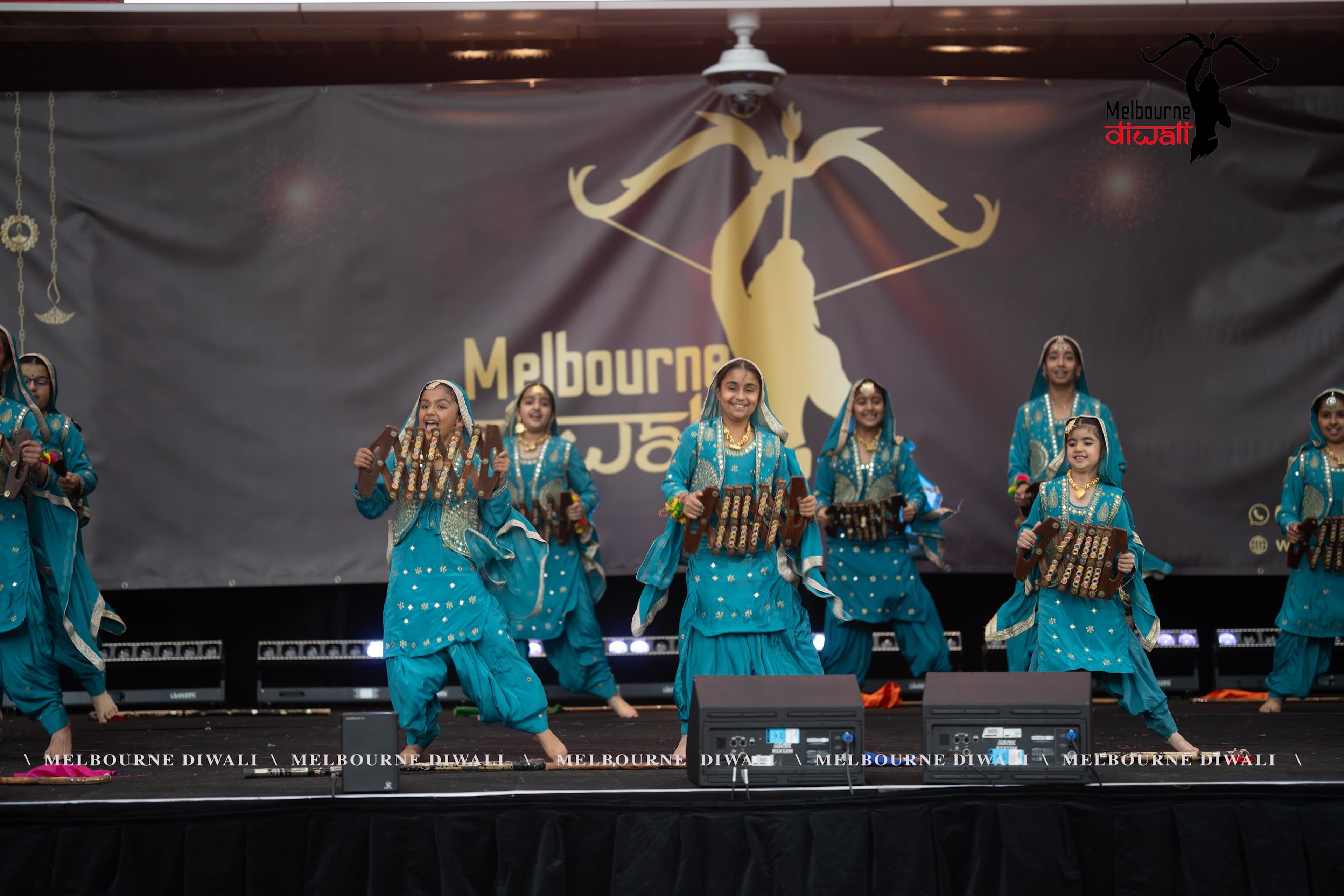 A Punjabi folk troupe in turquoise costume performing on the main stage at Melbourne Diwali 2025