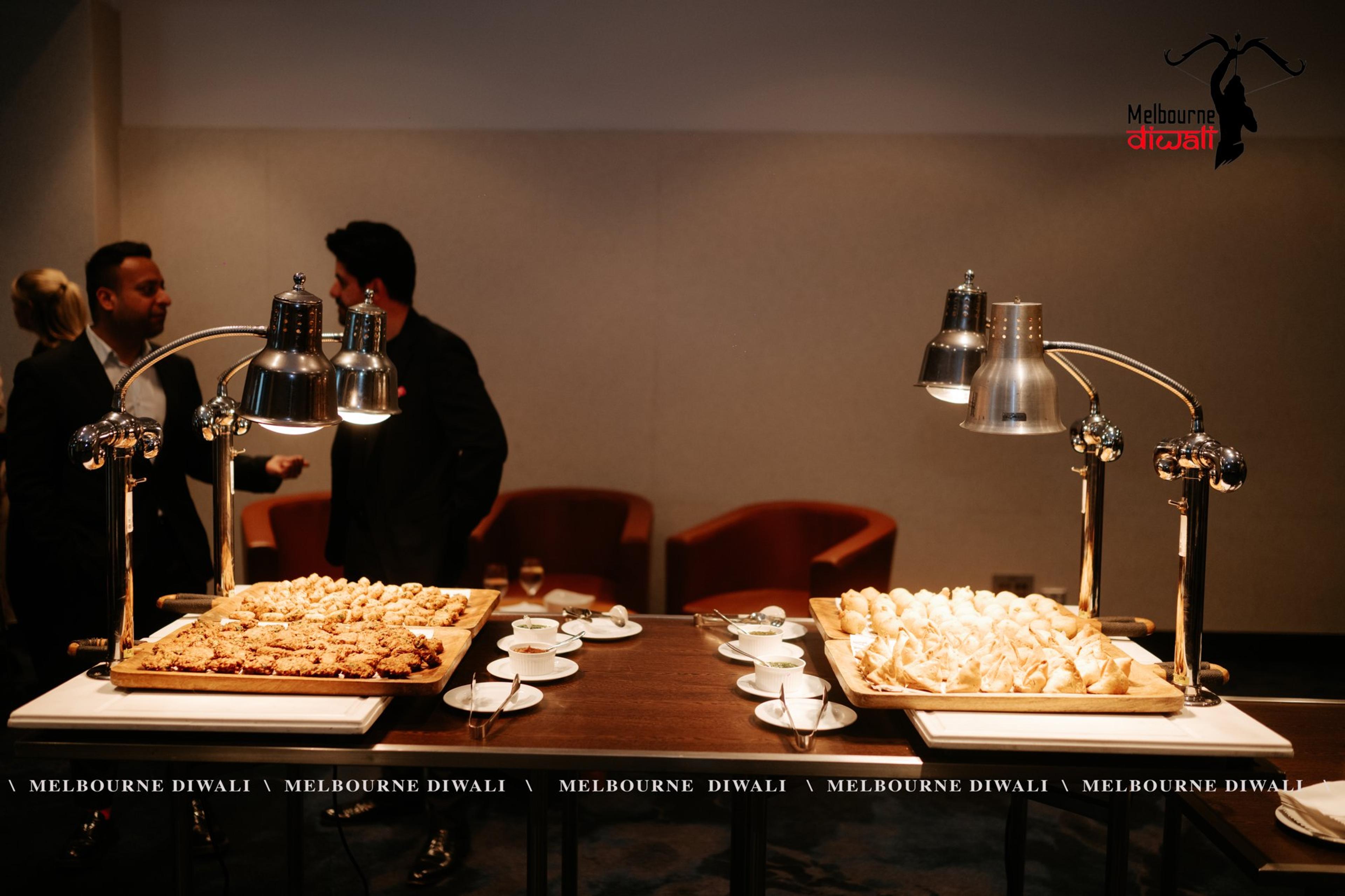 Samosas and snacks laid out under warming lamps