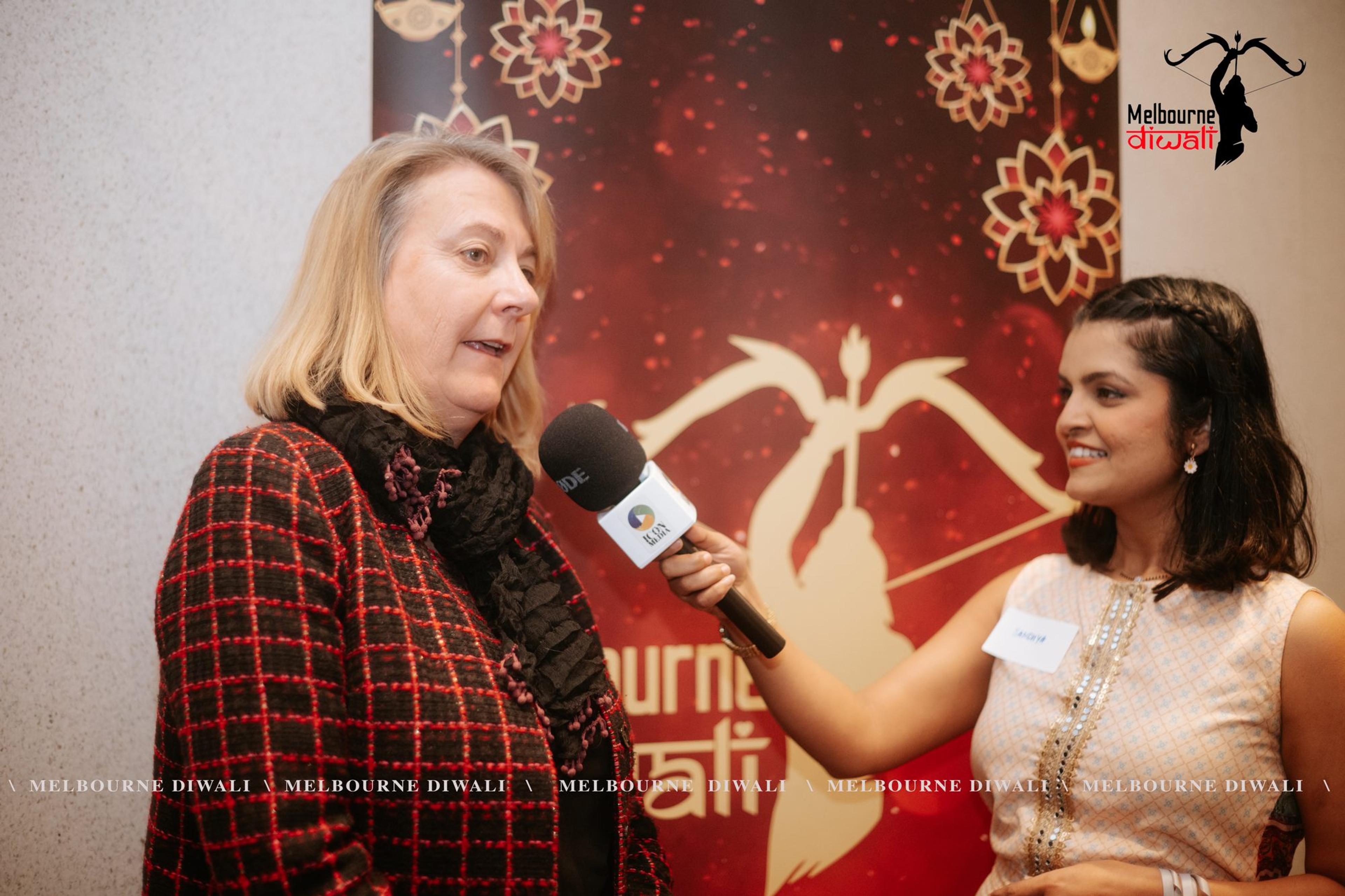 A guest is interviewed with a handheld microphone in front of the Melbourne Diwali media wall
