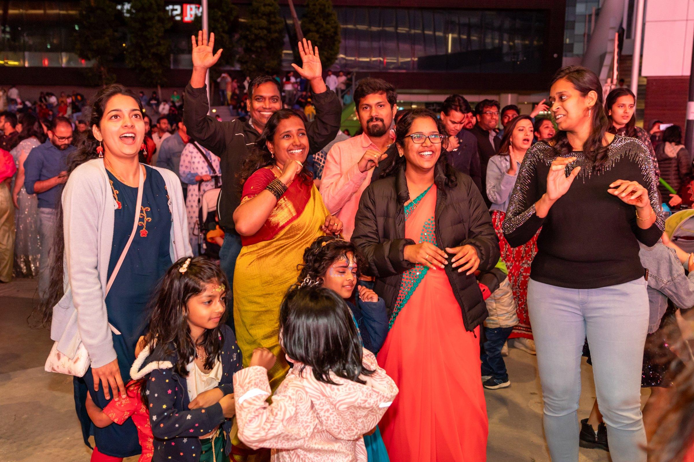 Families in saris and festive wear dancing and cheering with their children at Melbourne Diwali 2023, Docklands