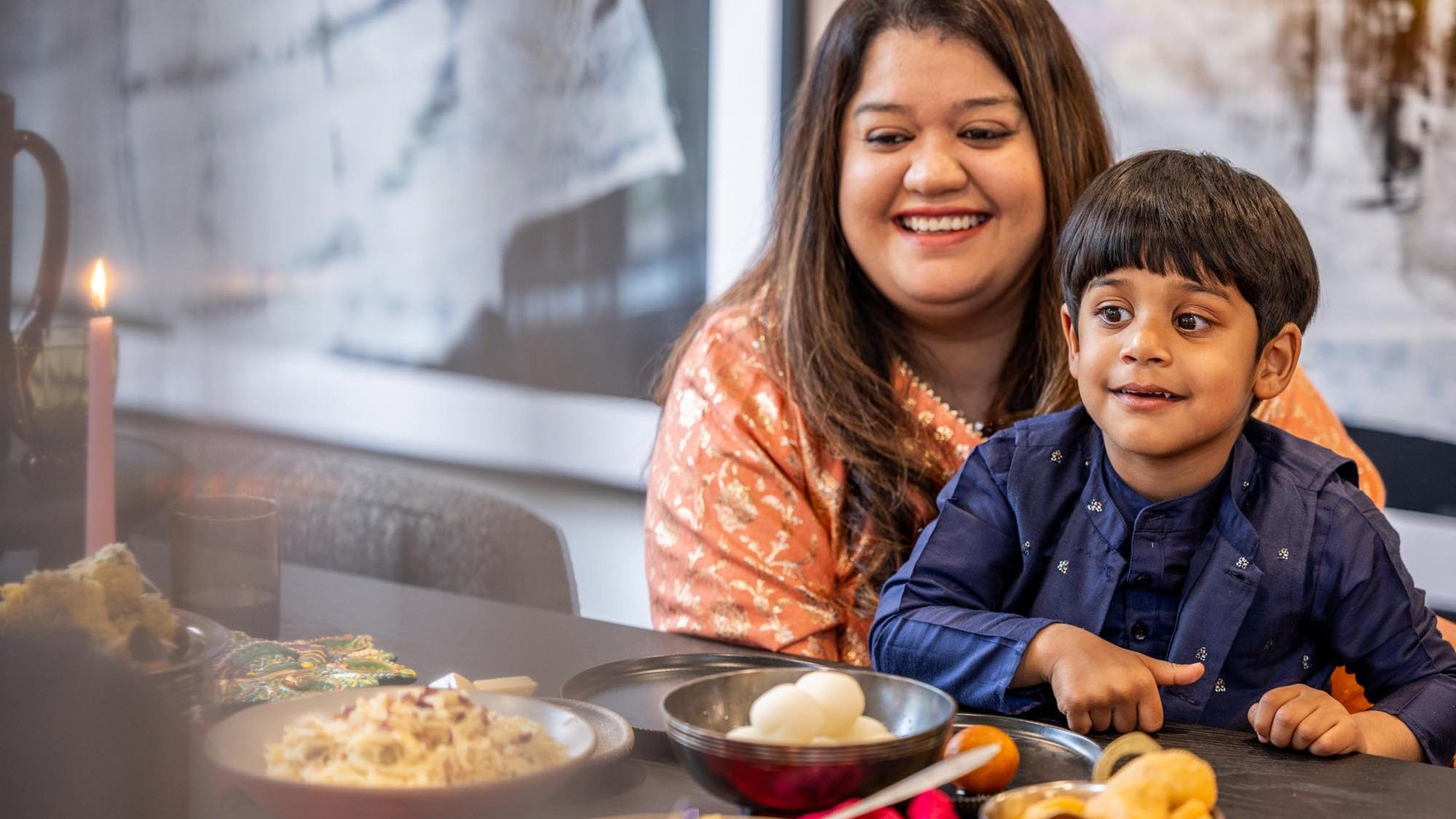 A mother and her young son smiling at a Diwali table set with sweets and candles