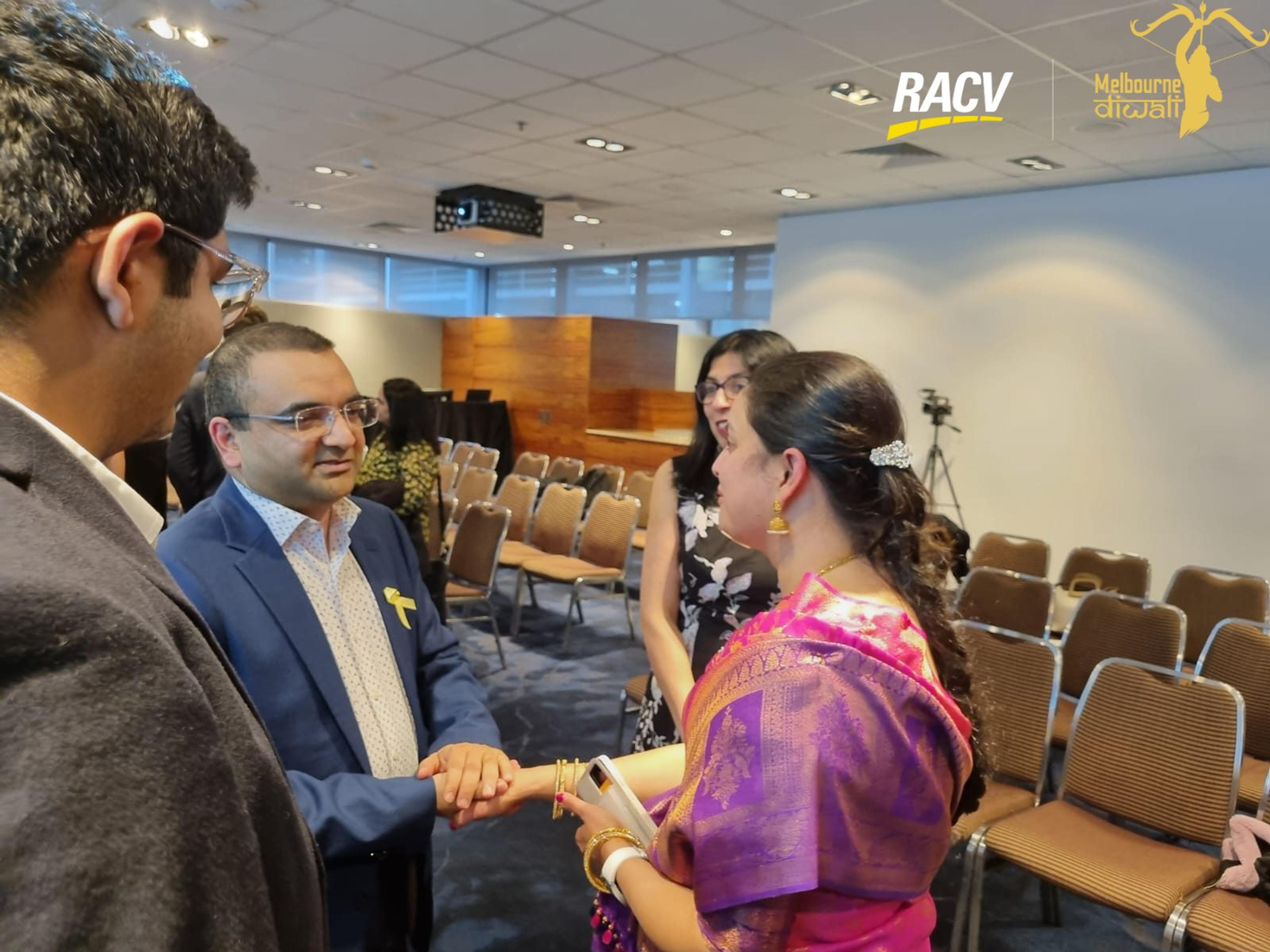 A guest in a purple saree shakes hands with another guest after the presentations
