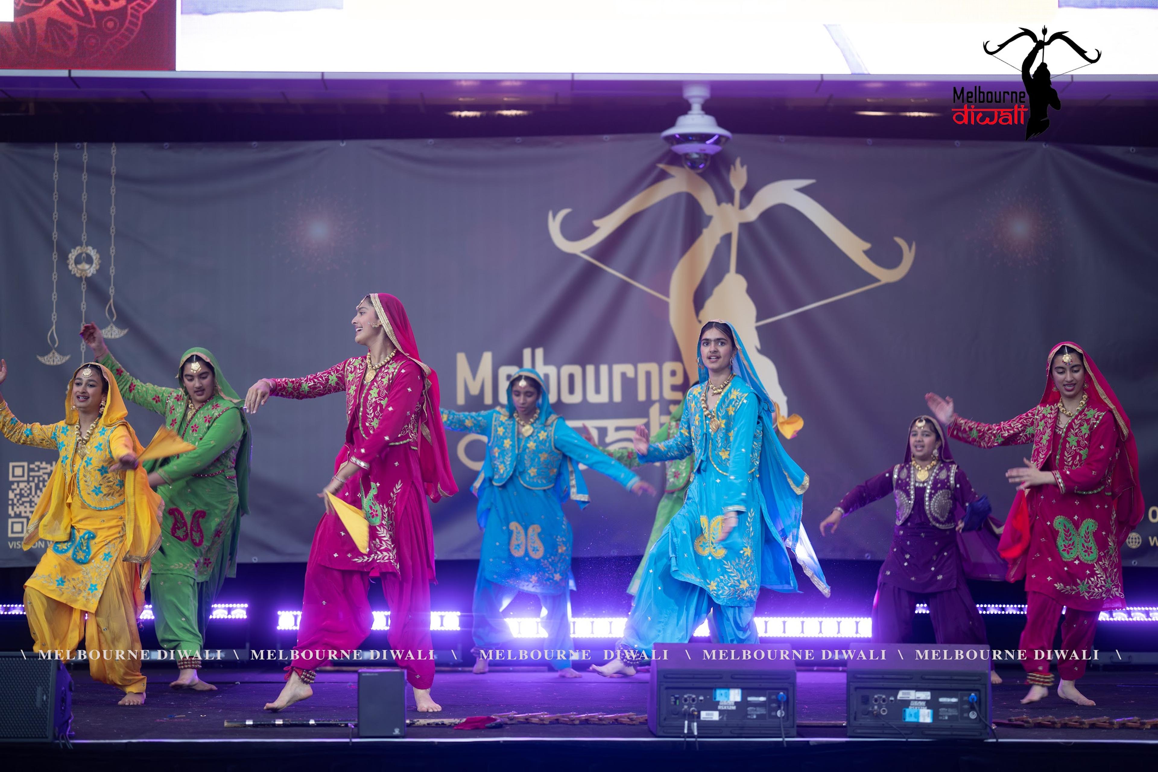 A dance group in brightly coloured traditional dress performing under stage lights at Melbourne Diwali 2025