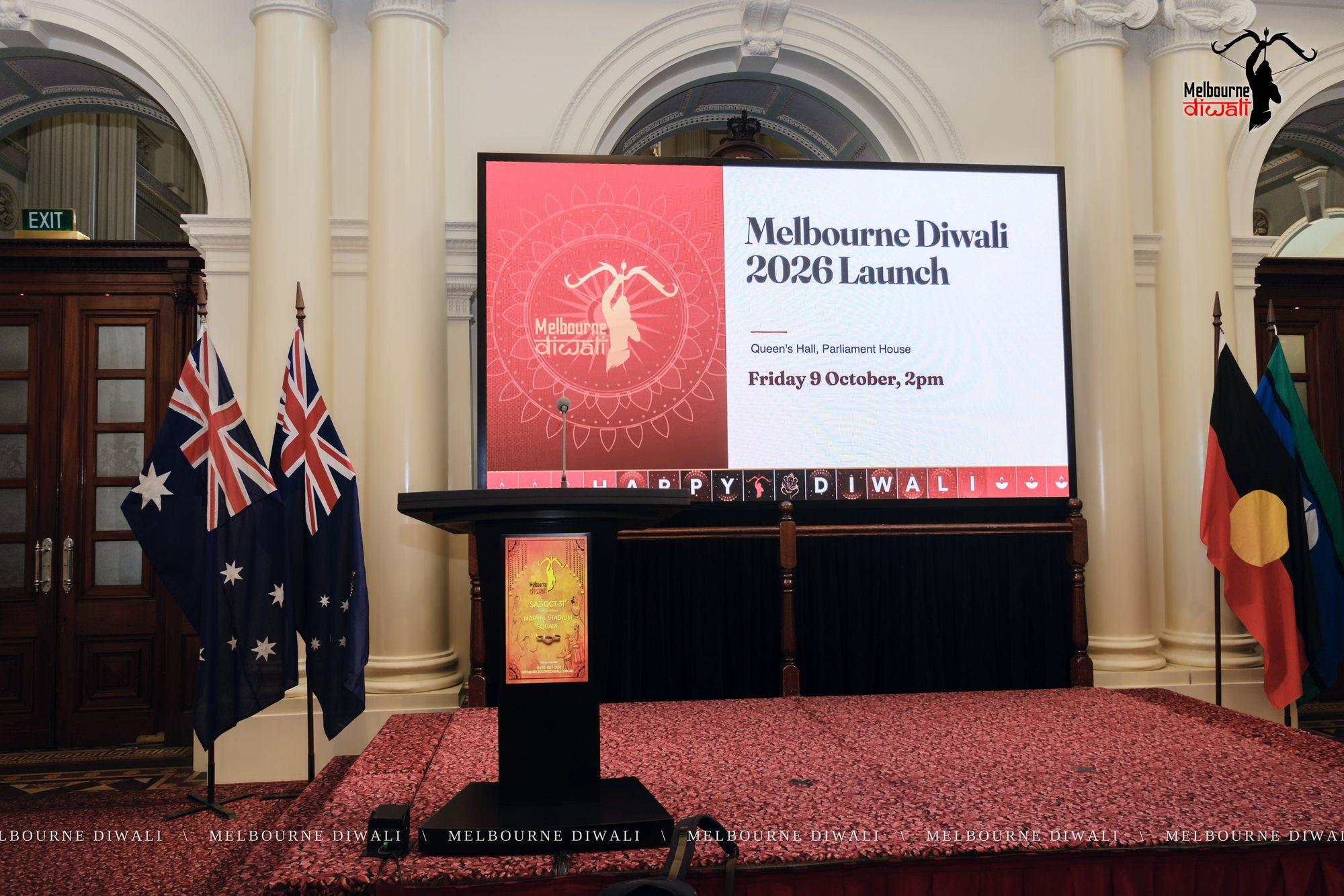 Queen's Hall set for the Launch: the lectern, flags and the Melbourne Diwali 2026 Launch screen