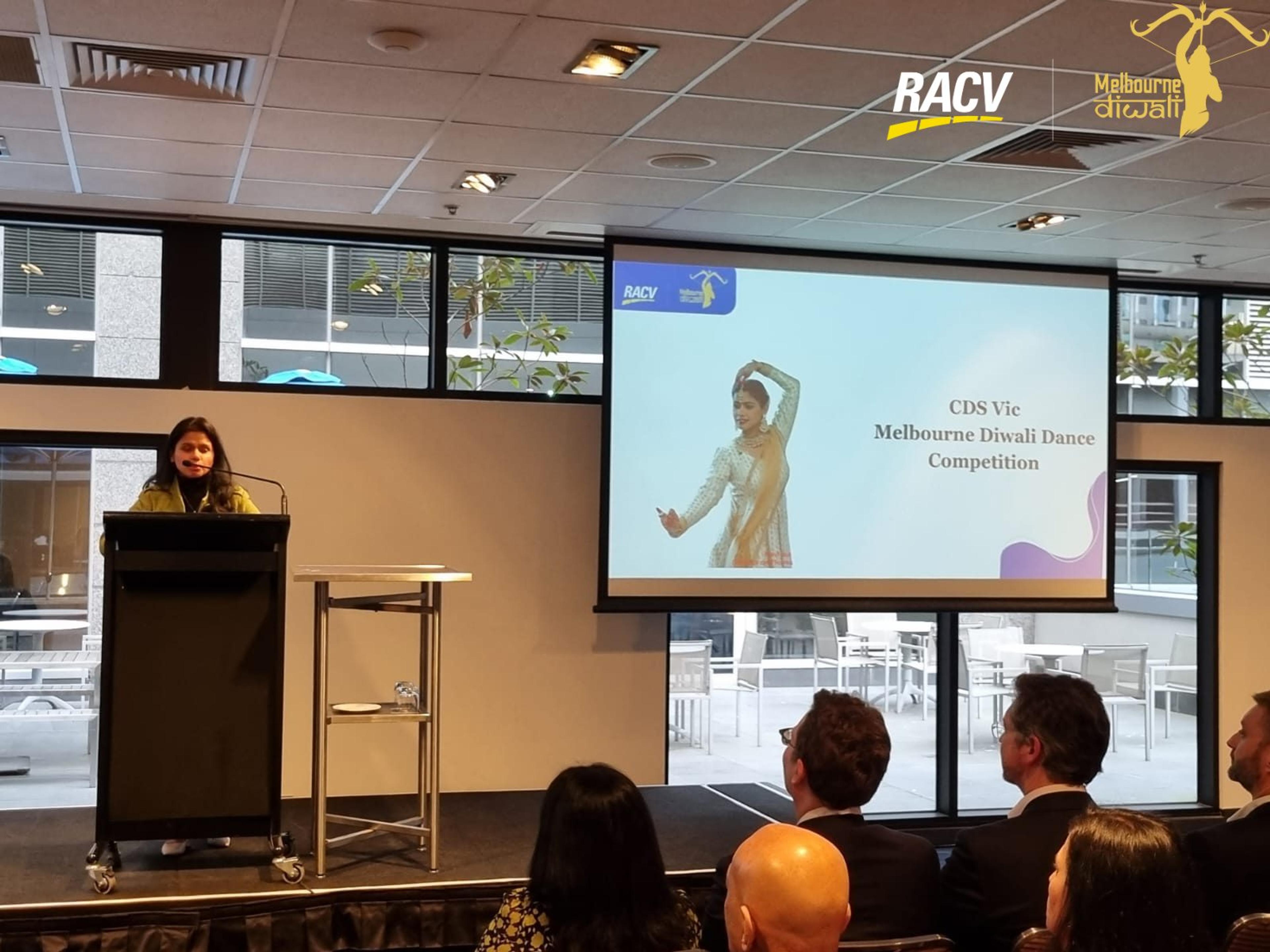 A speaker at the lectern beside the slide for the CDS Vic Melbourne Diwali Dance Competition