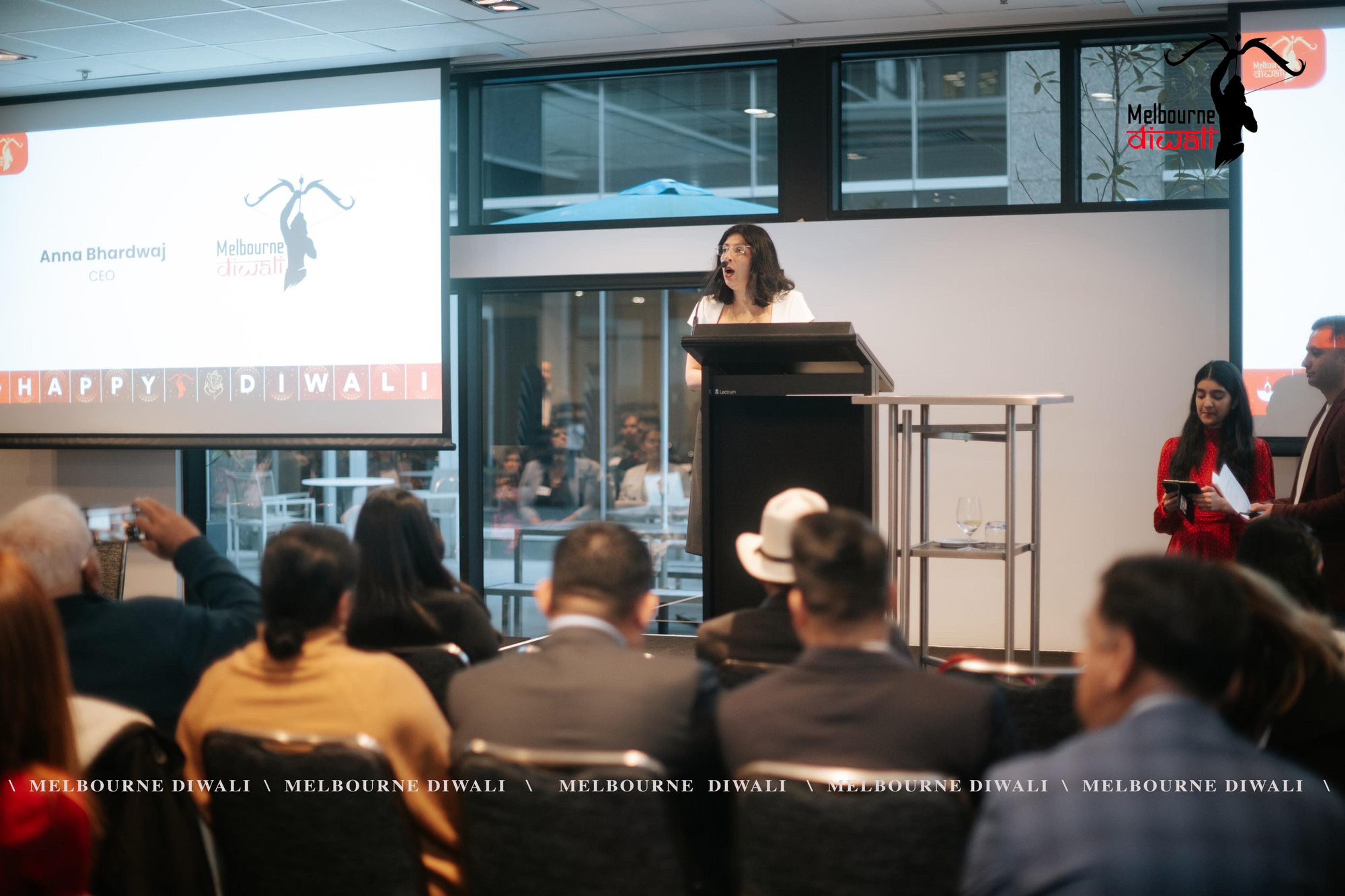 Anu Bhardwaj, CEO of Melbourne Diwali, speaks at the lectern beside her name slide as guests look on