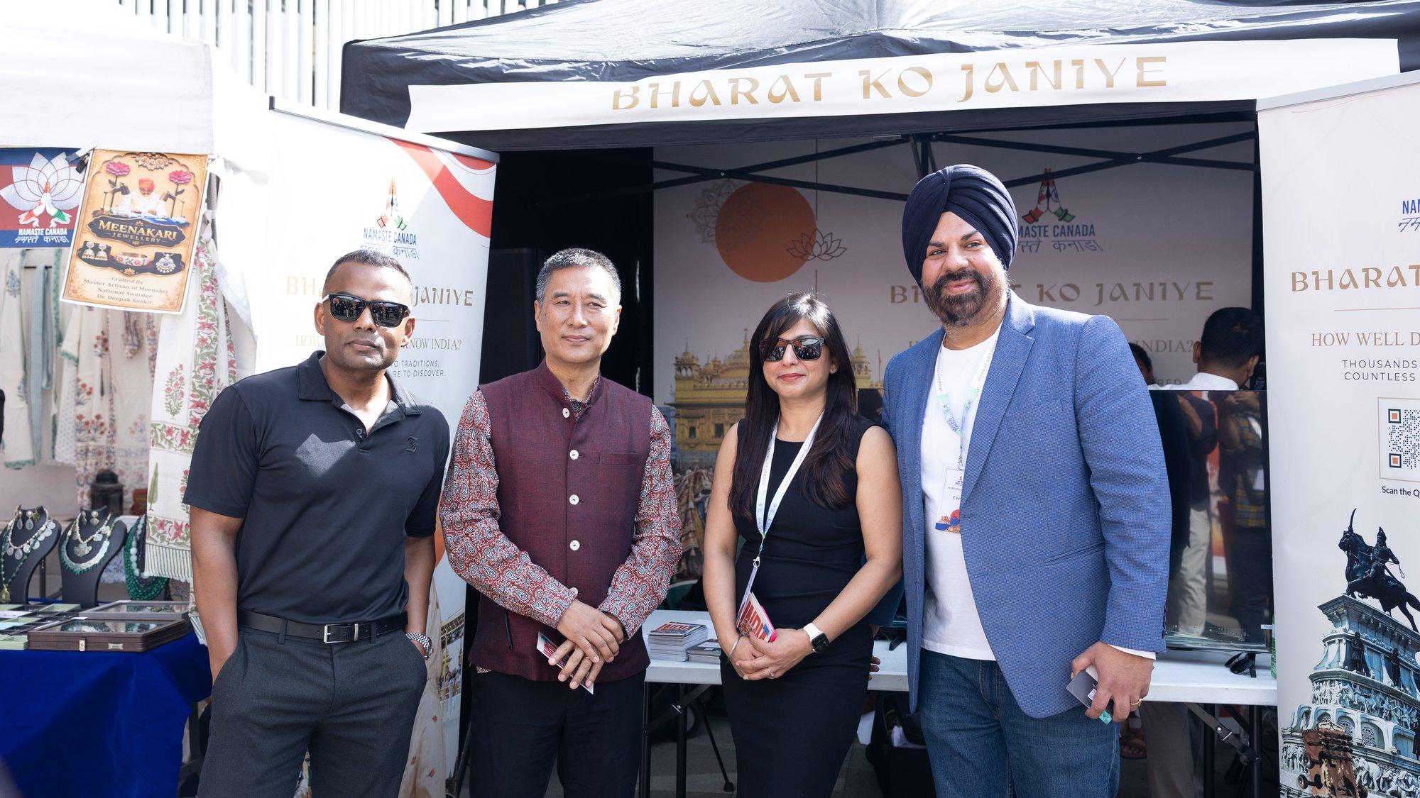 Four people standing in front of the Bharat Ko Janiye stall at an outdoor festival in Vancouver