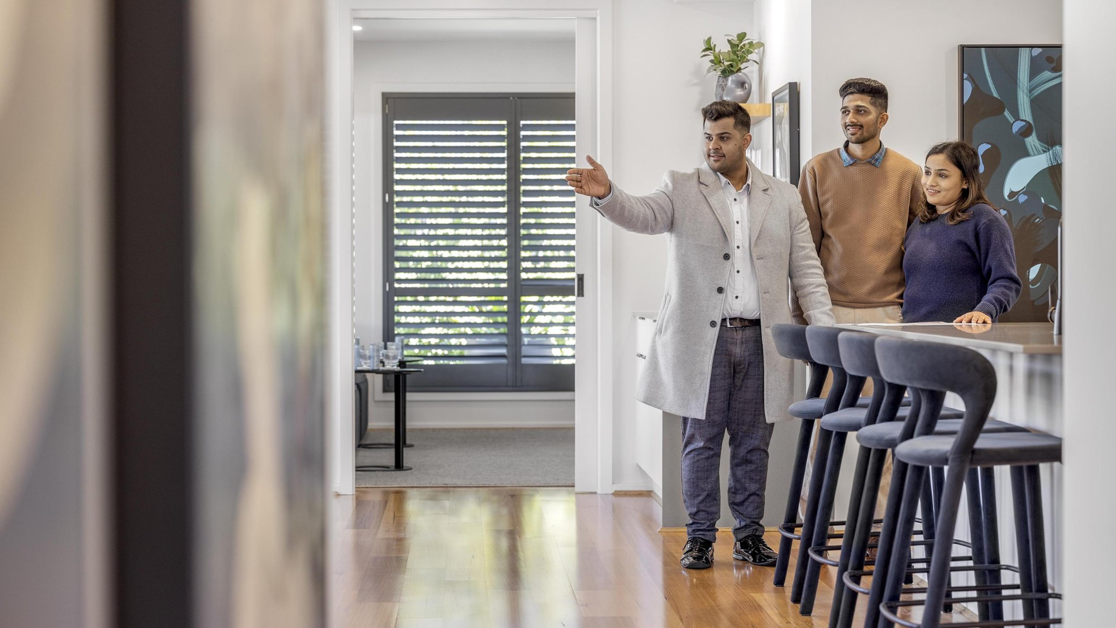 A family being shown through an open-plan home with a kitchen island and bar stools