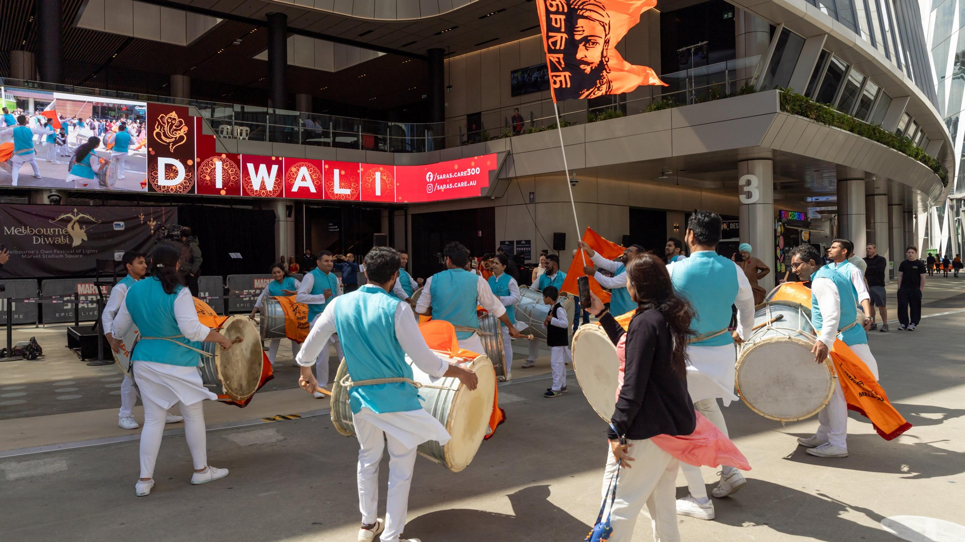 A dhol drumming group performing in Marvel Stadium Square beneath the Diwali screen