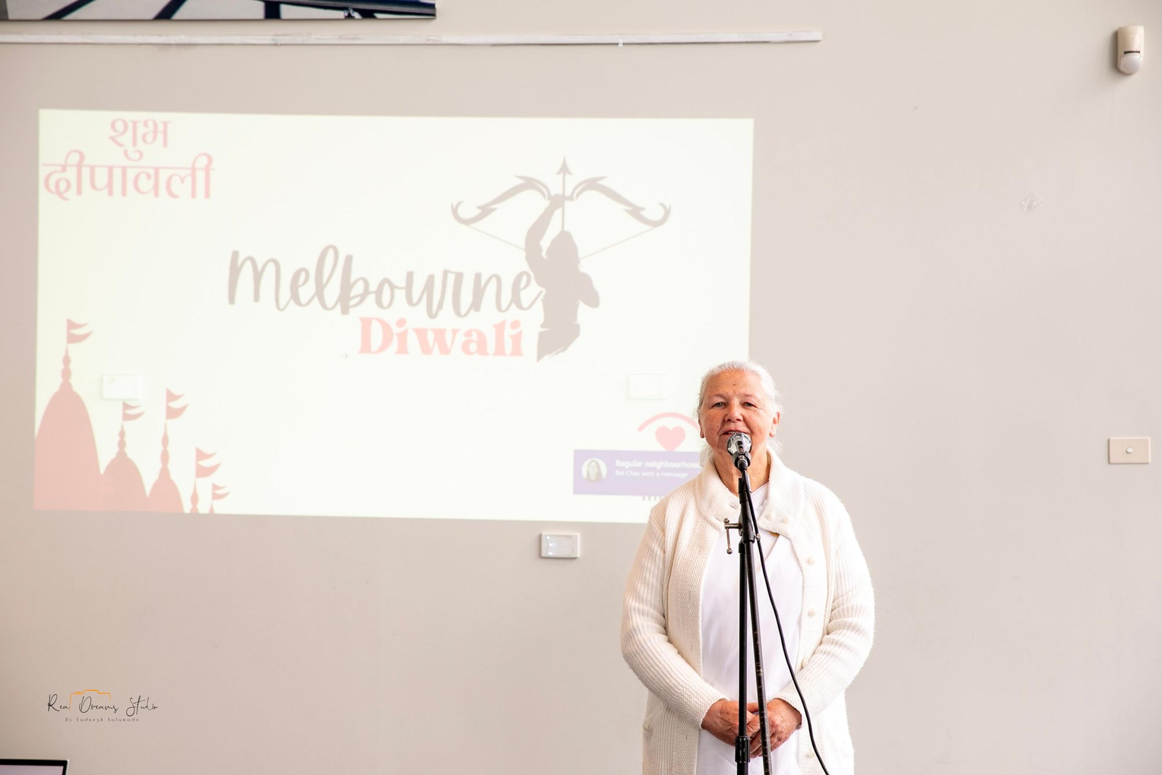 Sister Morni of the Brahma Kumaris gives the opening words in front of the Melbourne Diwali title slide