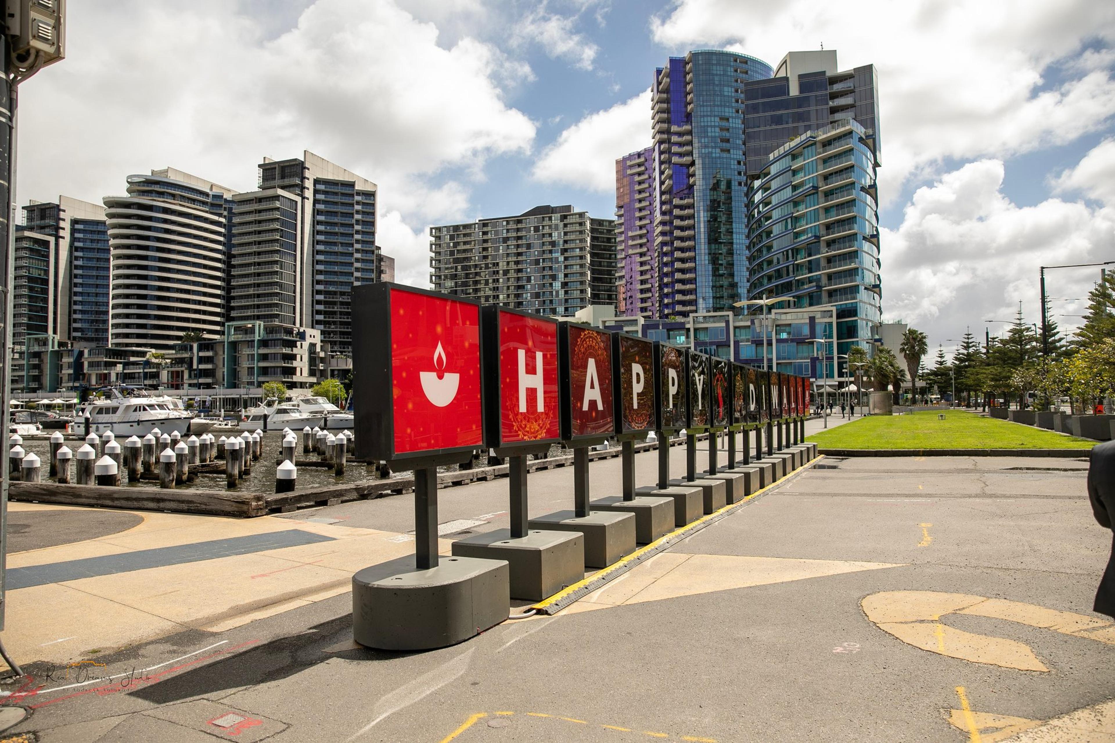 The illuminated HAPPY DIWALI letter sign on Harbour Esplanade, with Docklands towers behind