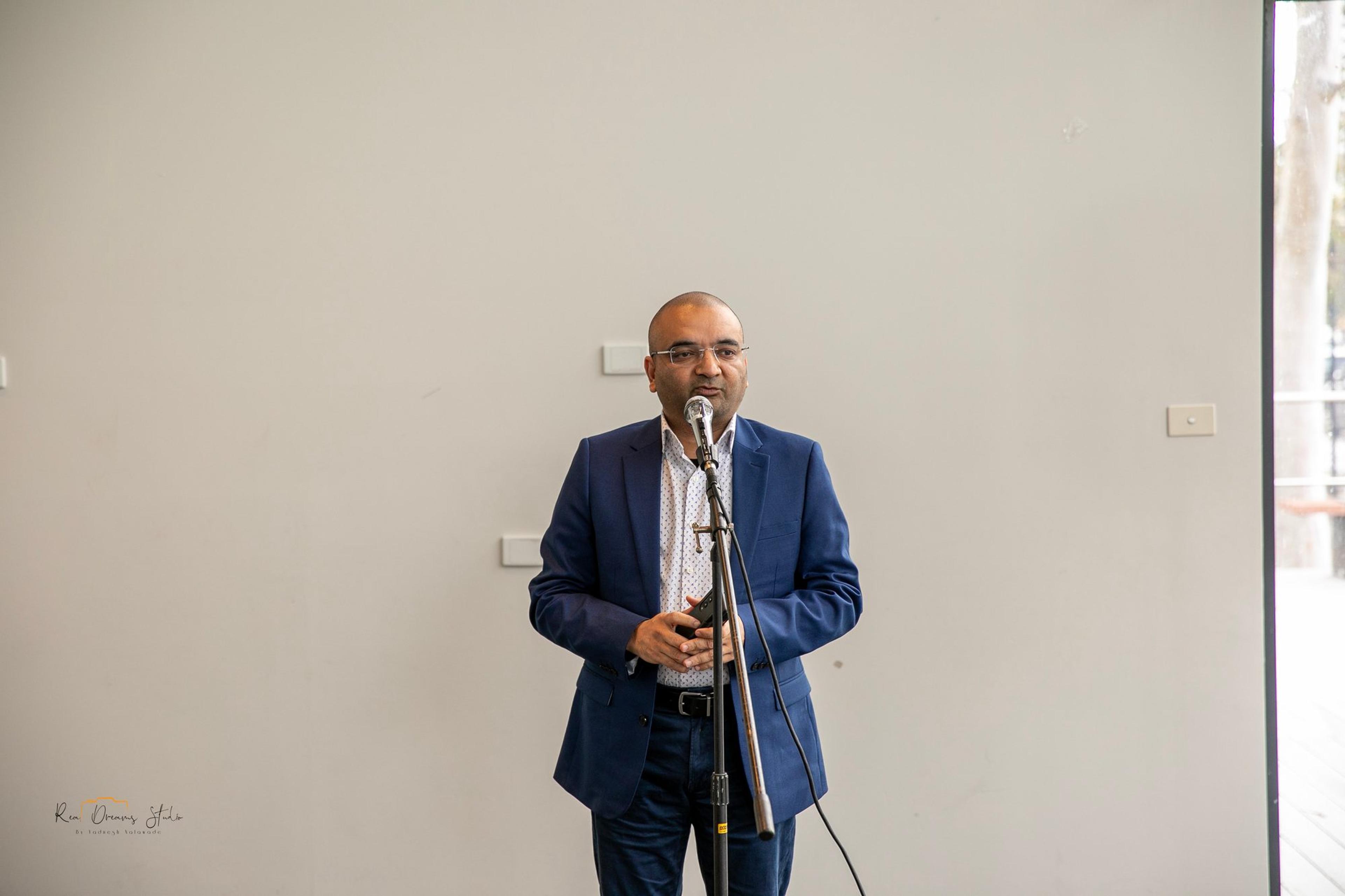 A man in a blue suit speaks at the microphone