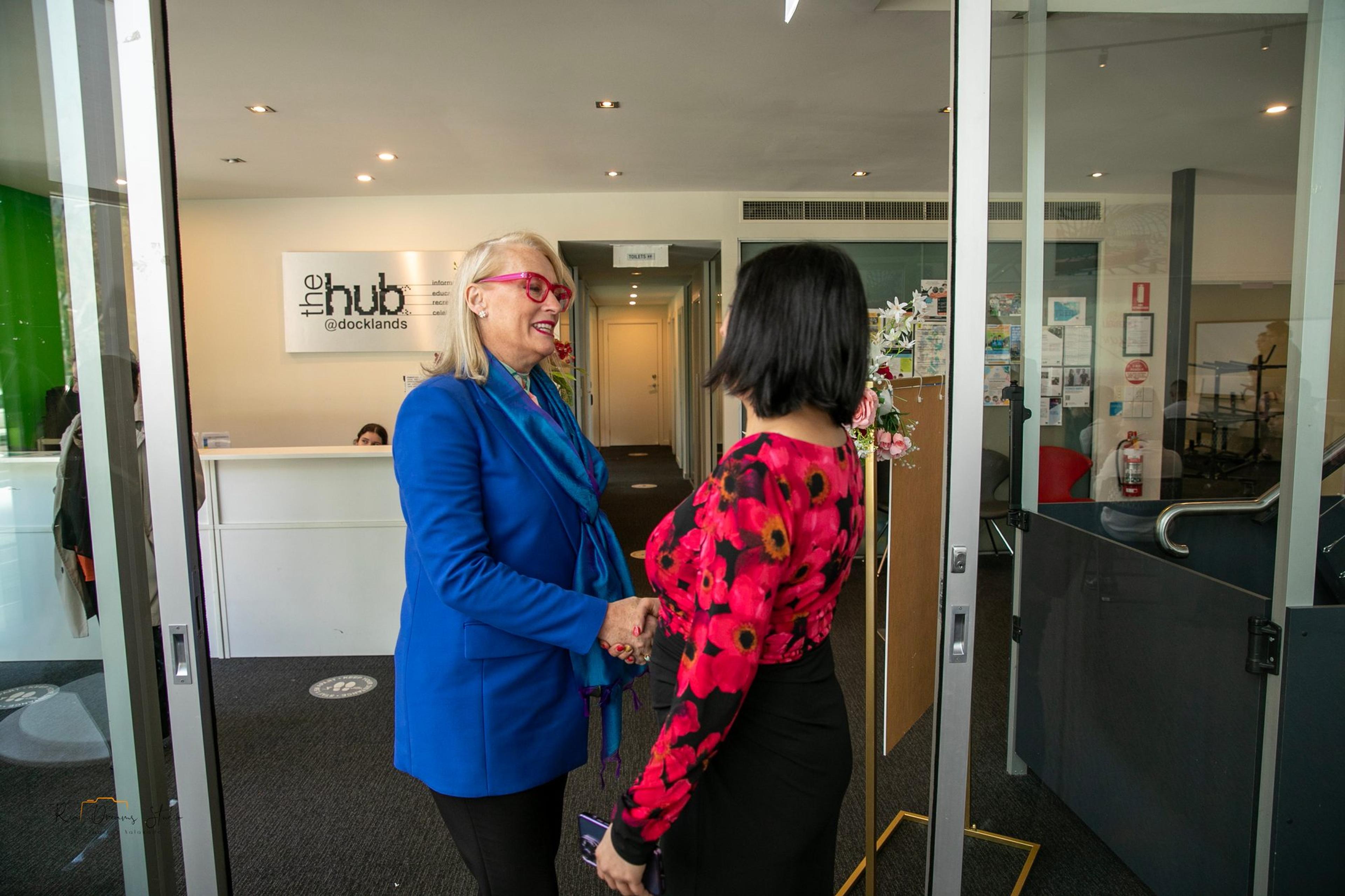 A guest in a blue jacket is welcomed at the door of The Hub