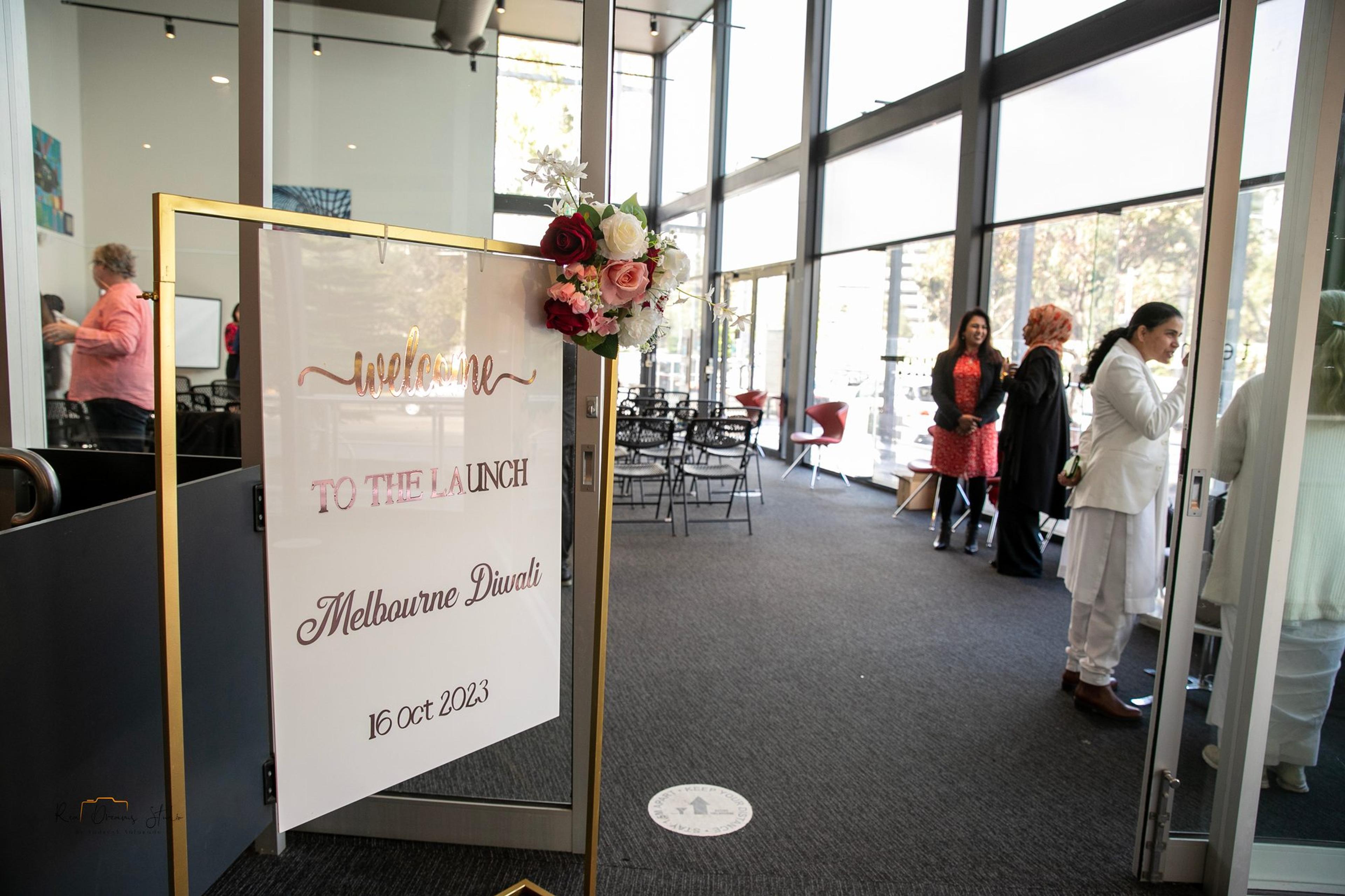 A gold easel sign reading 'Welcome to the Launch, Melbourne Diwali, 16 Oct 2023' as guests arrive at The Hub, Docklands
