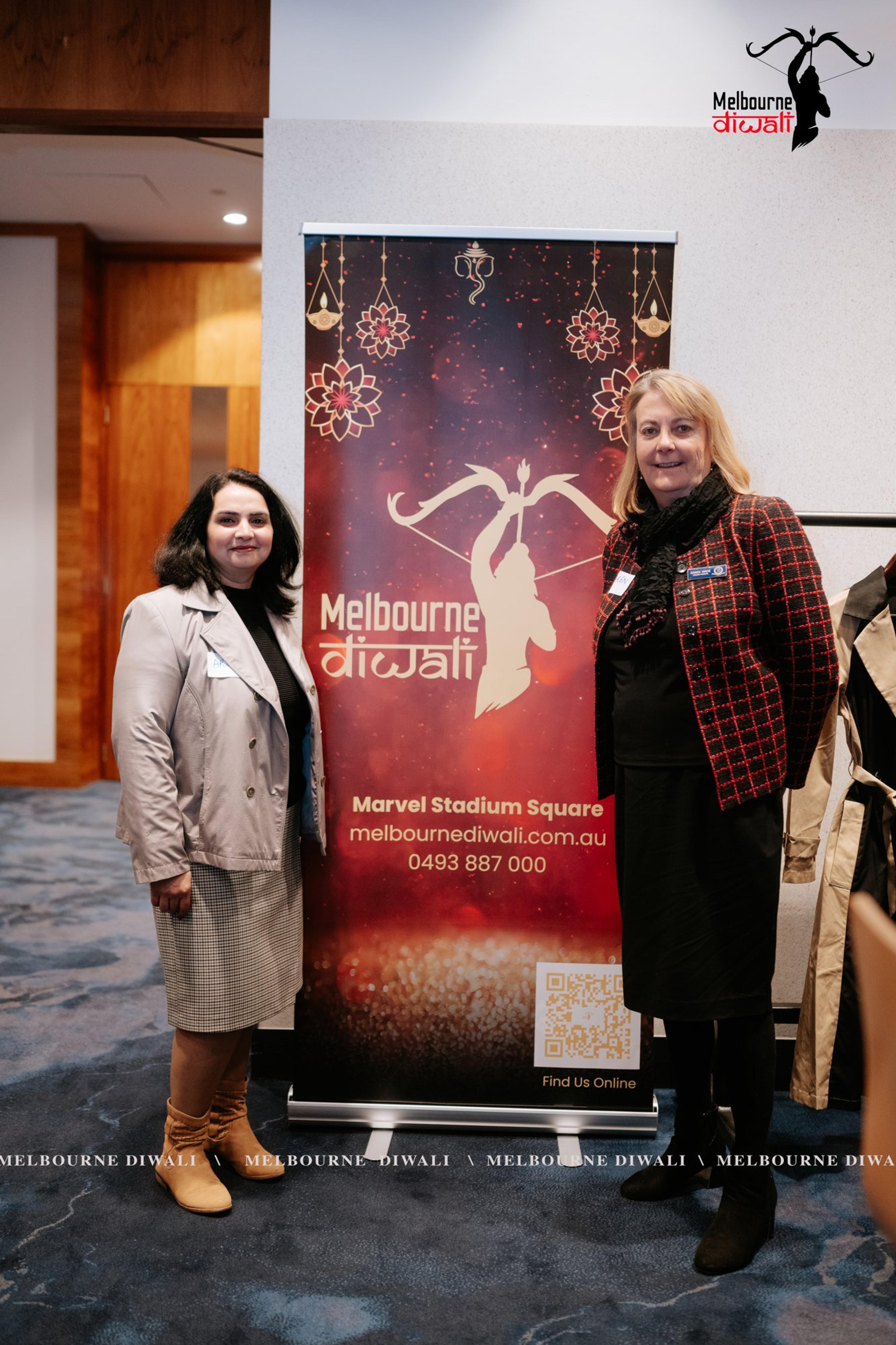 Two guests stand beside the Melbourne Diwali pull-up banner