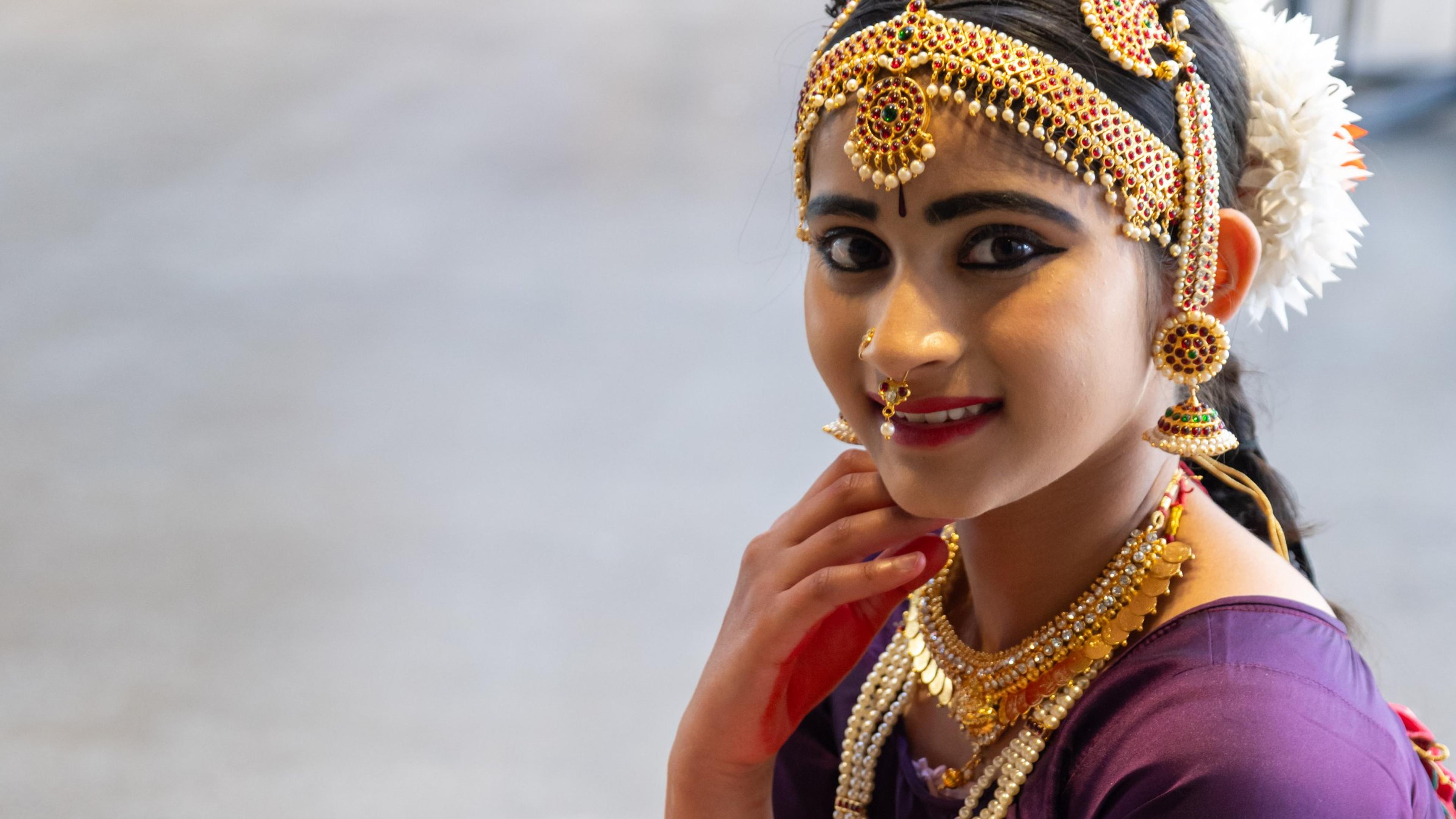A classical dancer in a purple costume and gold jewellery smiling at Melbourne Diwali